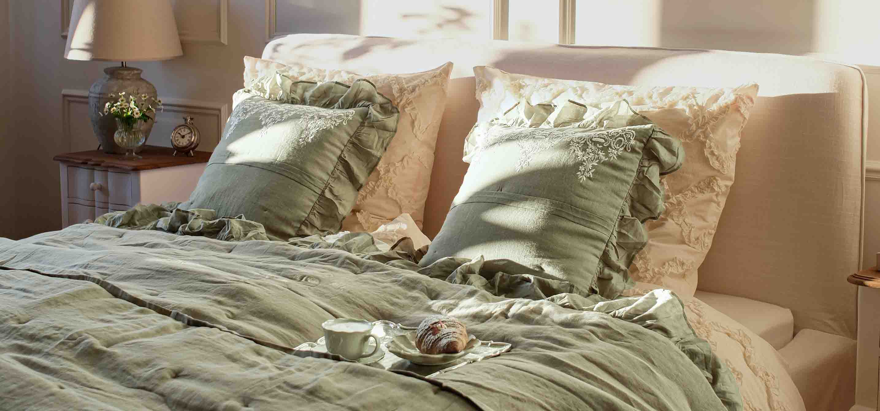 Linge de lit vert avec coussins à volants dans une chambre lumineuse avec lampe et horloge