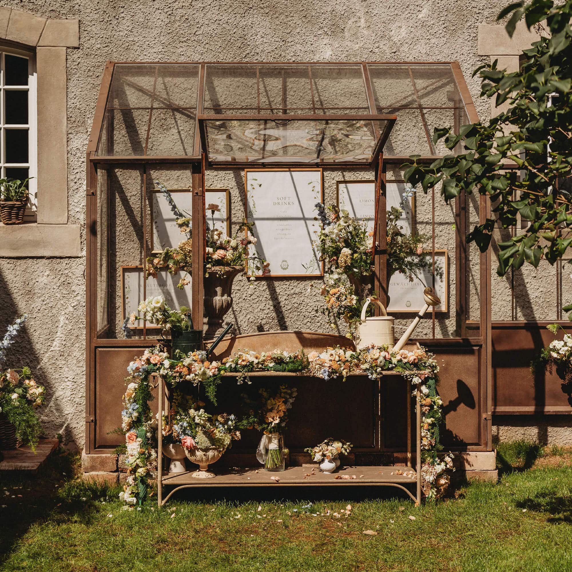 Table de jardin en métal décorée de fleurs et arrosoirs devant une serre en verre