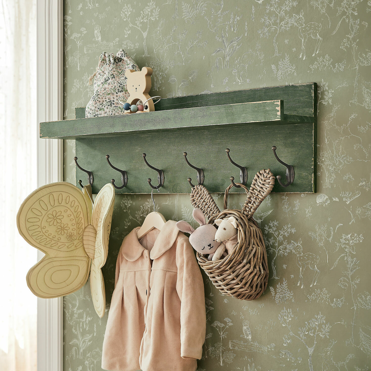 Étagère murale Hoboken Étagère murale verte en bois avec crochets, manteau enfant et panier en osier avec peluches sur fond de papier peint animalier
