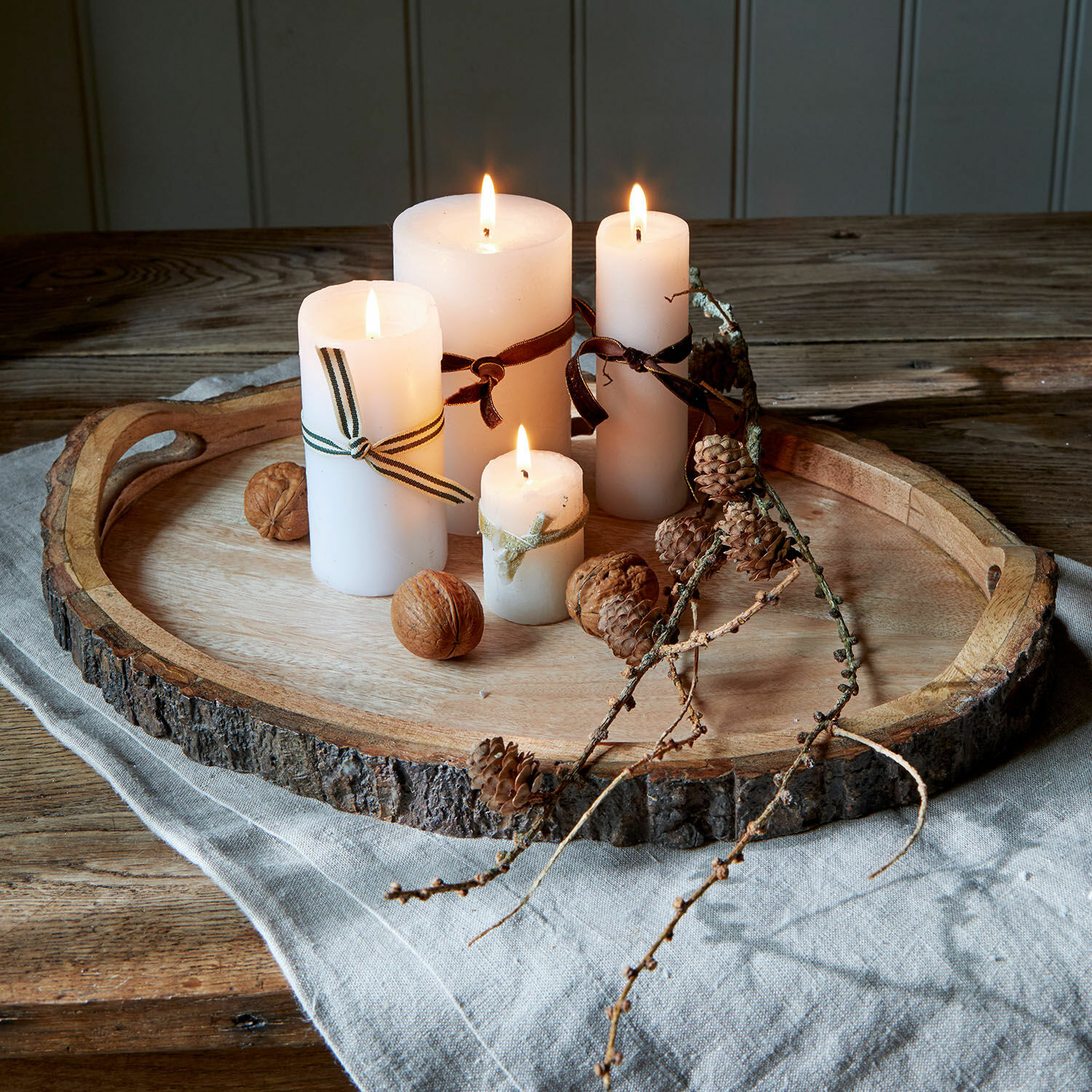 Plateau Danice Plateau en bois naturel avec écorce, quatre bougies blanches allumées et décoration de noix et pommes de pin