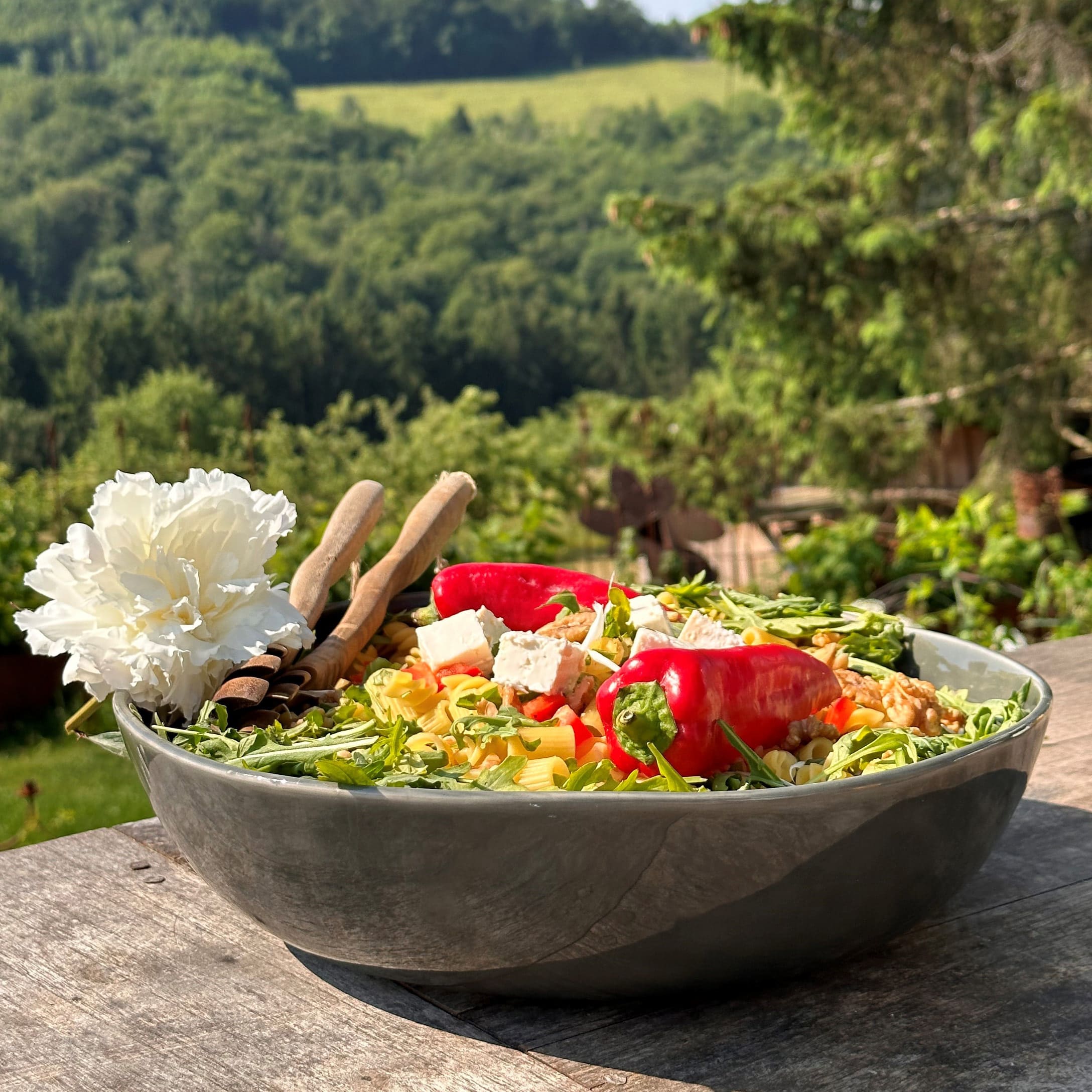 Grand bol en céramique avec salade, poivrons rouges, feta et roquette sur table en bois en extérieur