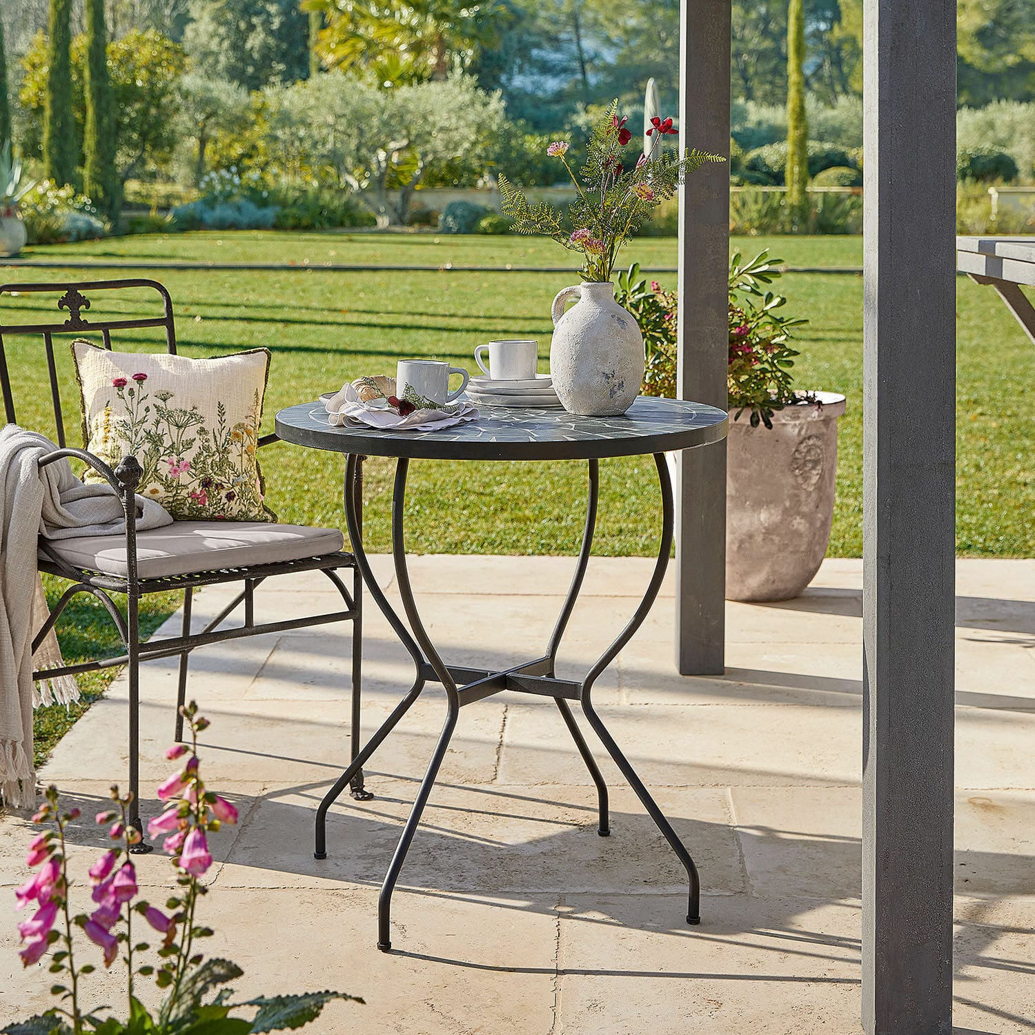Table Ballaigues Table de jardin ronde avec cadre en métal et plateau en mosaïque gris sur terrasse ensoleillée