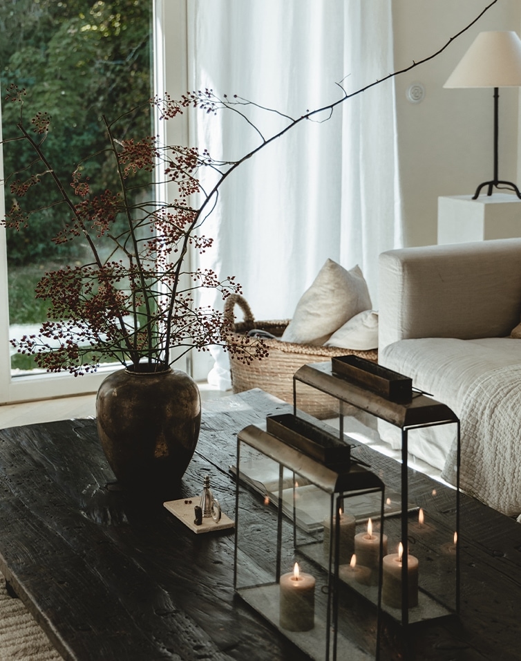 Table en bois noir rustique avec lanternes en métal et vase à branches dans un salon lumineux
