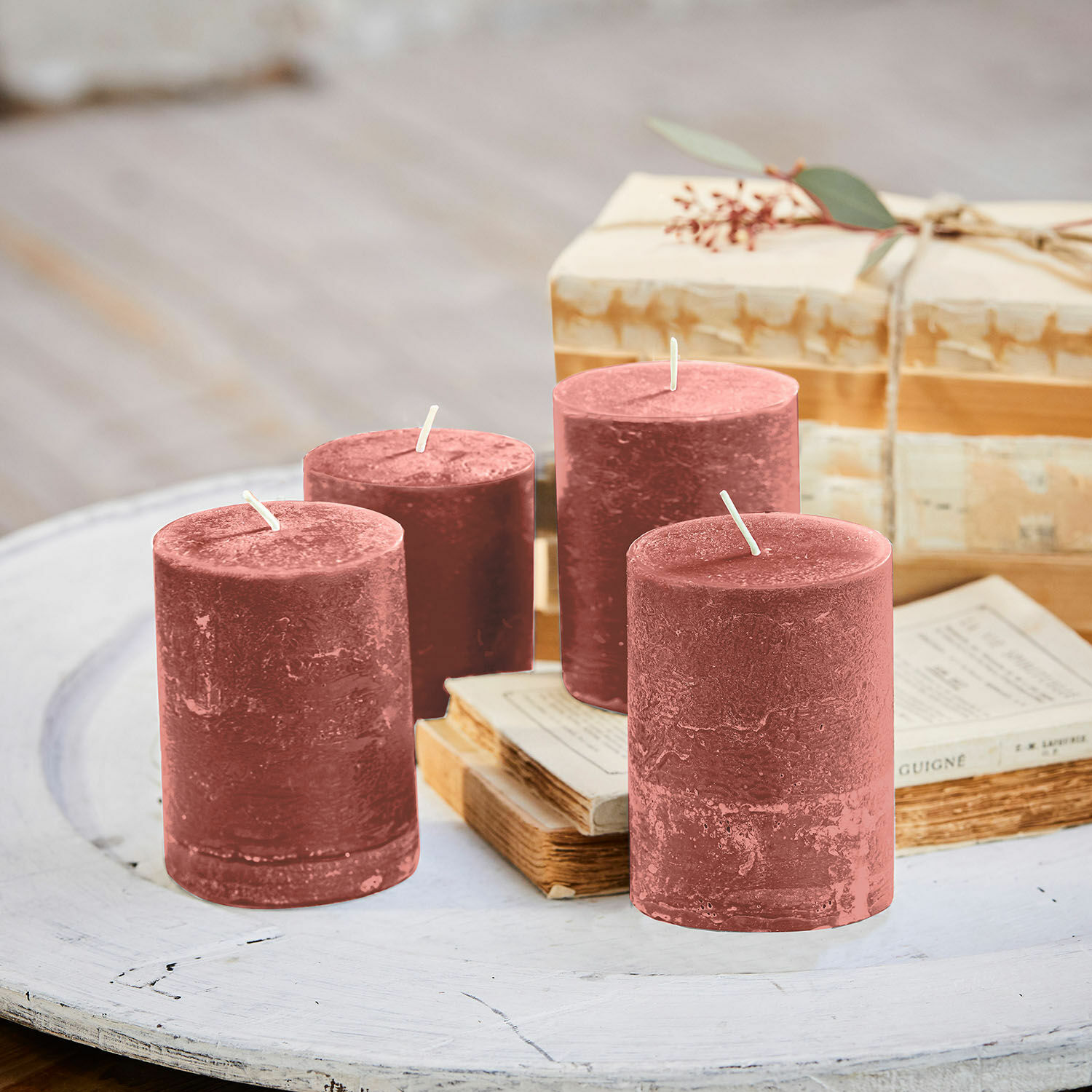 Lot de 4 bougies Virrans Ensemble de quatre bougies rouges en cire sur une table en bois blanc avec des livres anciens