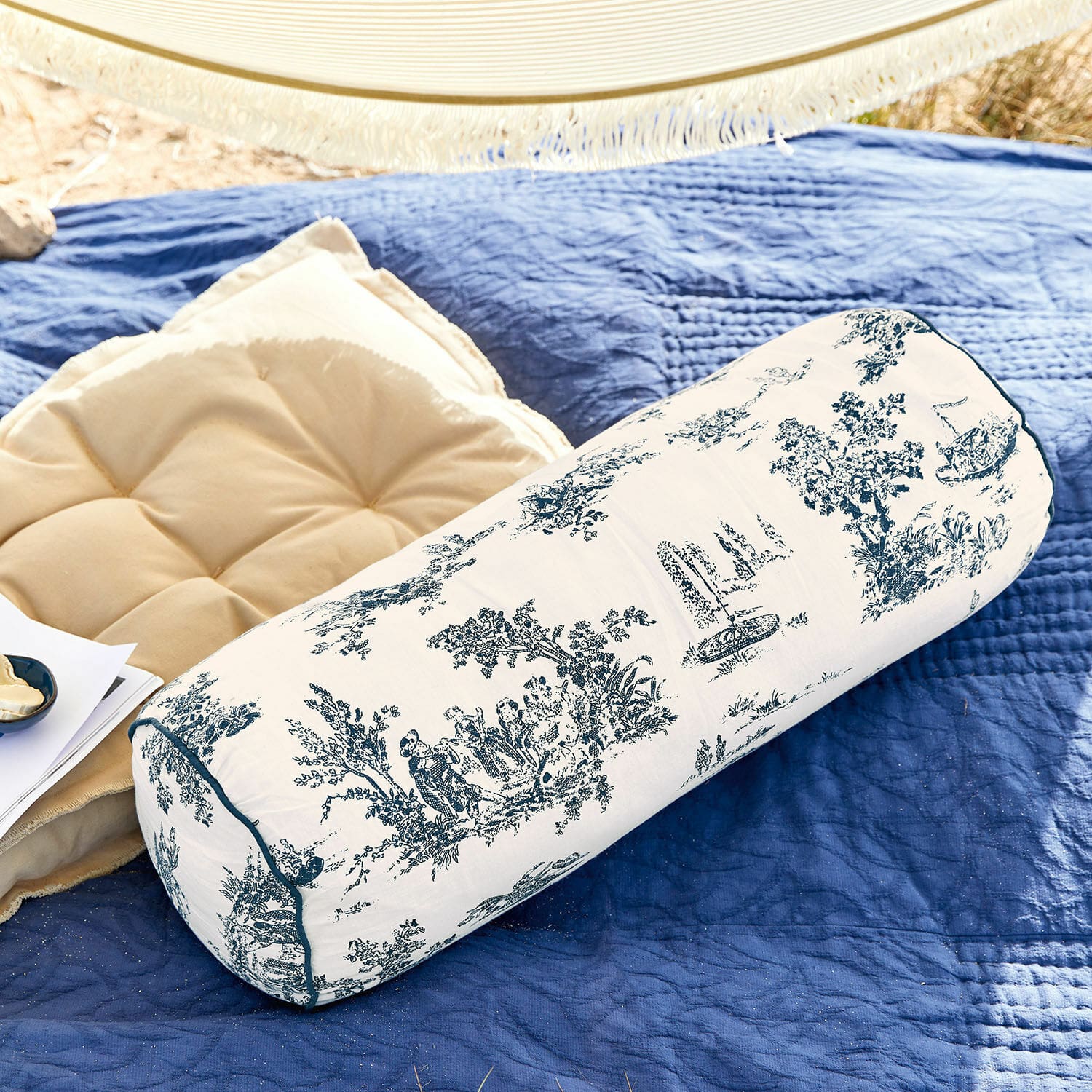 Cale-nuque Simone Coussin cylindrique en coton blanc à motifs bleus sur une couverture bleue avec coussin beige à côté