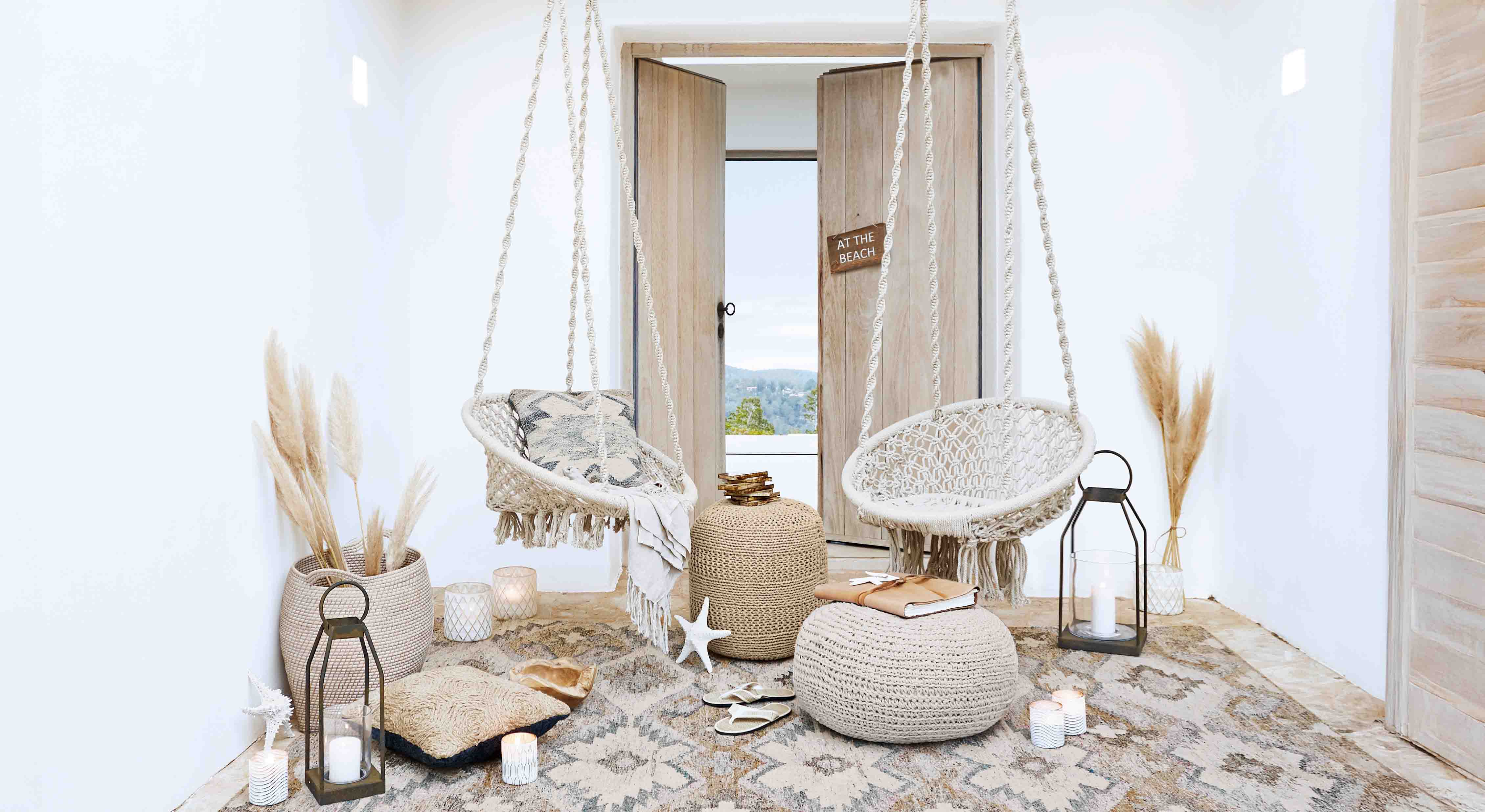 Salon cosy avec fauteuils suspendus en macramé blanc et décorations naturelles style bohème