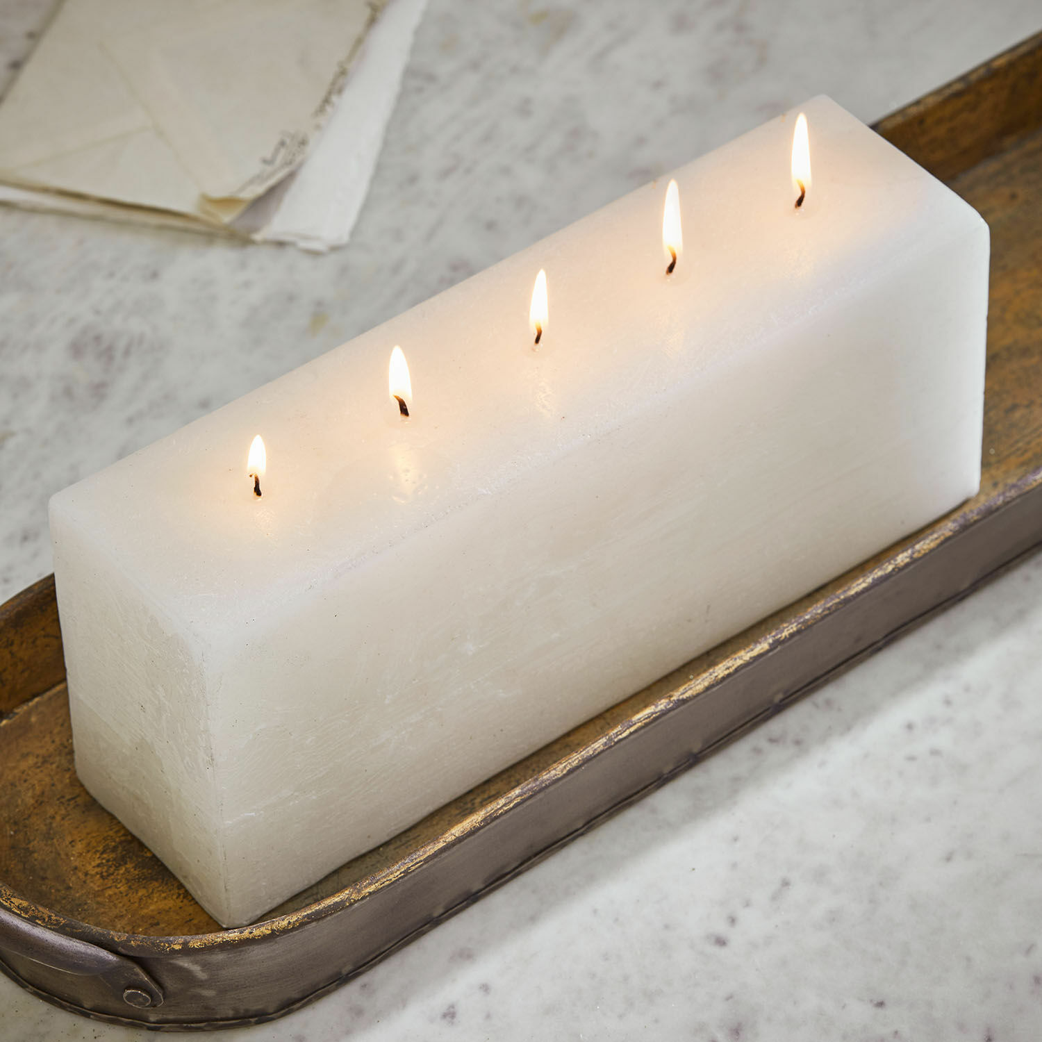 Bougie Thalara Bougie rectangulaire blanche avec cinq mèches allumées sur un plateau en métal décoratif