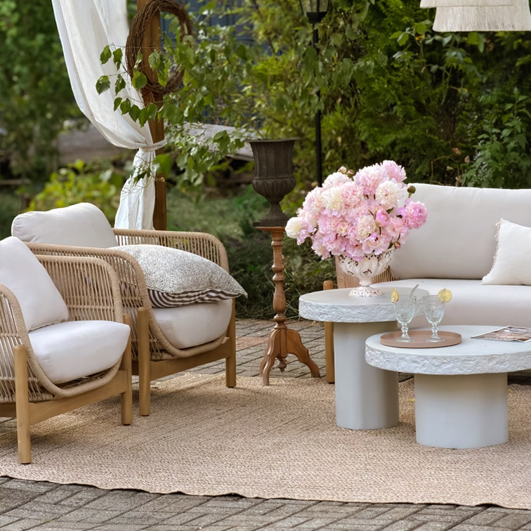Ensemble de mobilier de jardin avec coussins clairs, fauteuils en osier et tables basses en béton sur tapis en jute