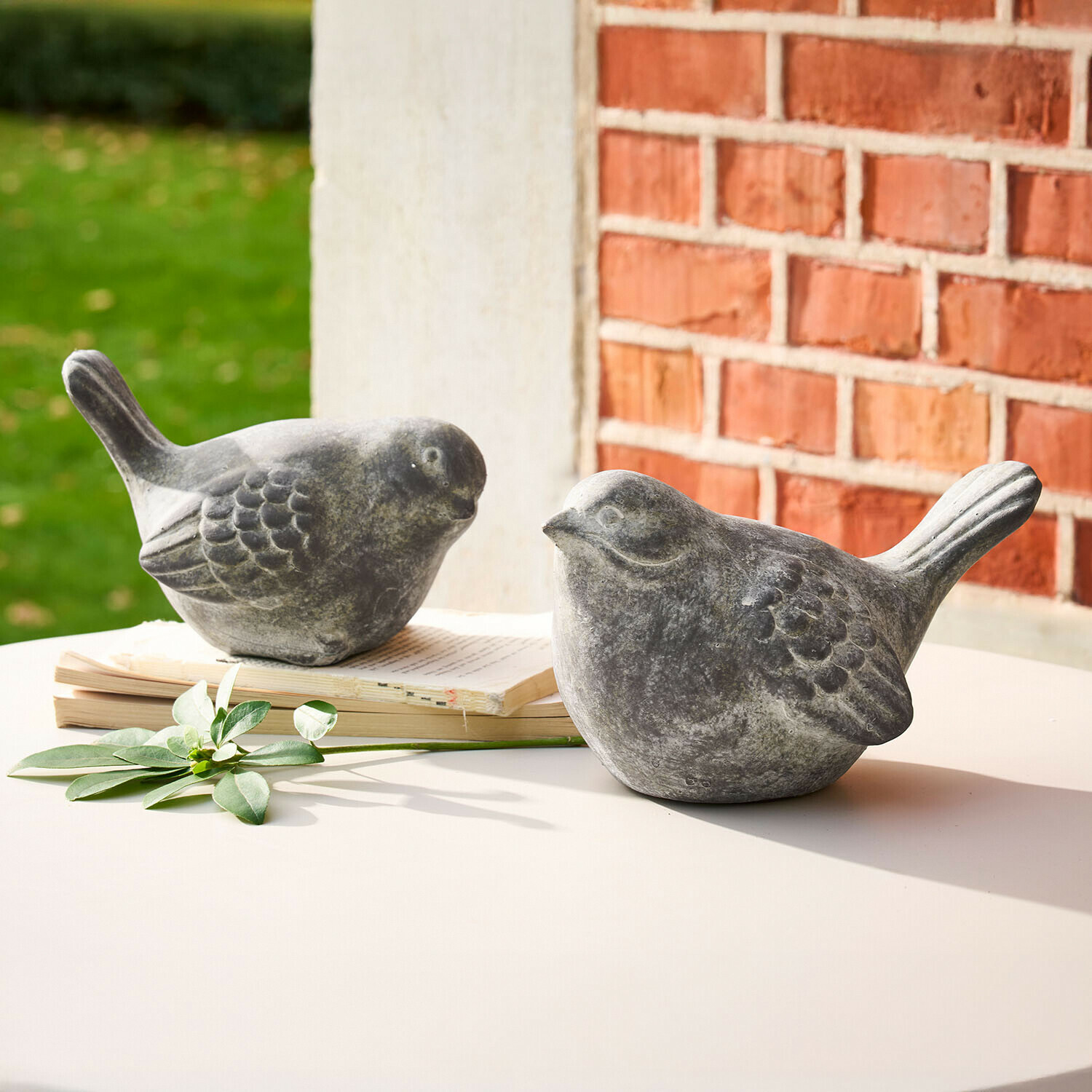 Deux figurines d'oiseaux décoratives en pierre grise sur une table blanche avec un livre et une feuille verte