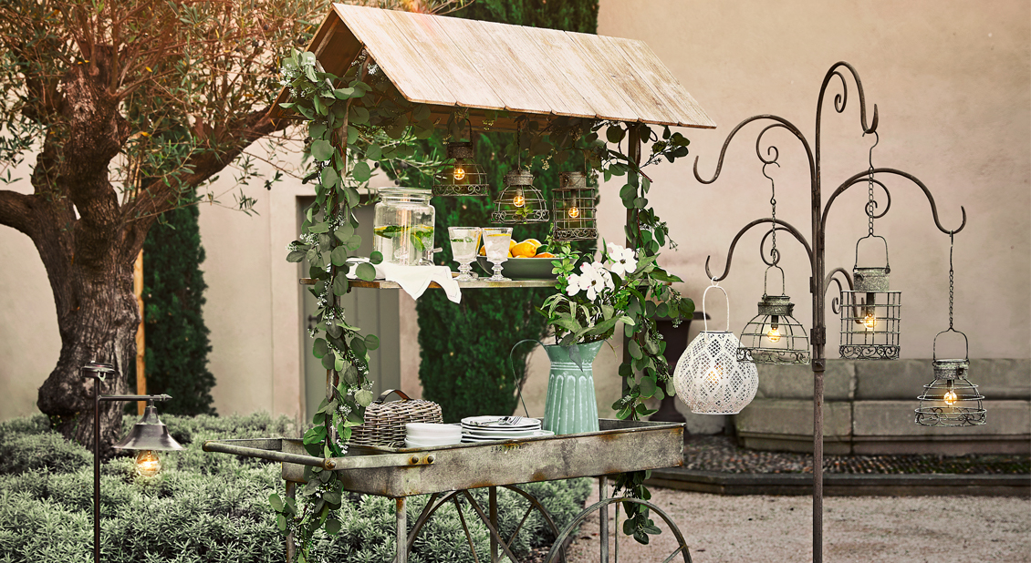 Chariot de jardin en métal rustique avec lanternes et feuillage vert, décoration extérieure élégante