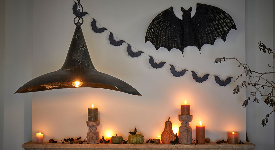 Décoration d'Halloween avec lampes noires, bougies allumées et guirlande de chauves-souris sur mur clair