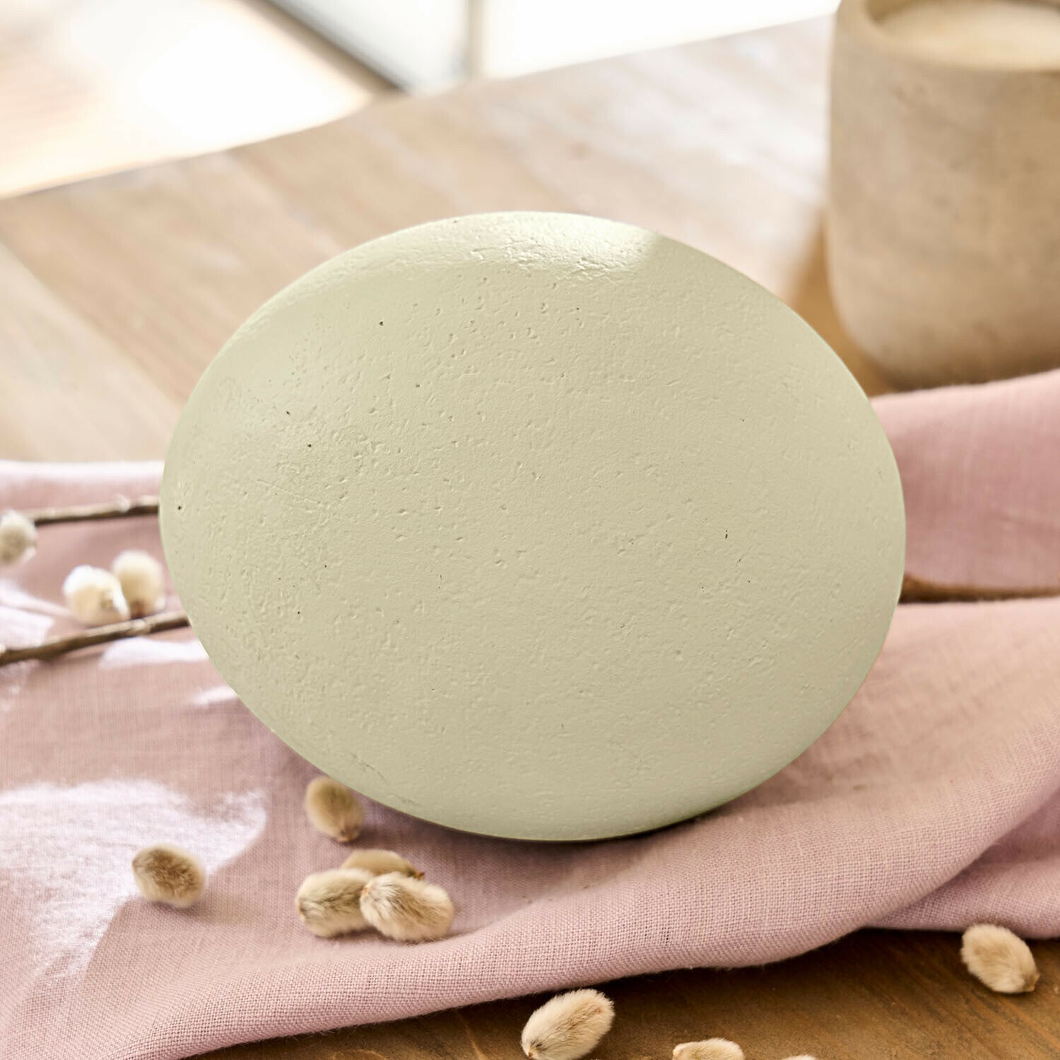 Œuf décoratif Fauverine Œuf décoratif en céramique mate couleur crème posé sur un tissu rose pour décoration intérieure