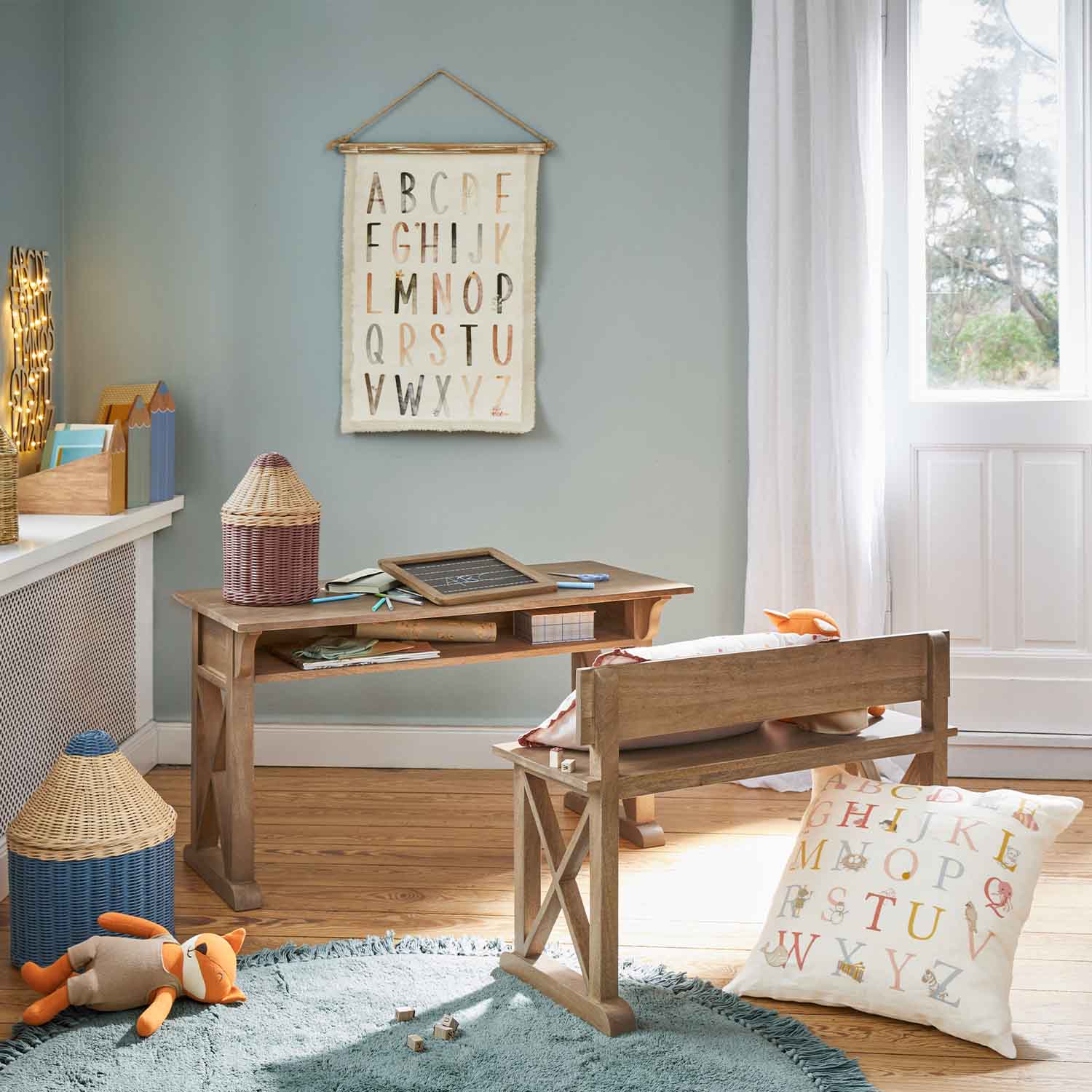 Bureau et banc en bois dans une chambre d'enfant avec coussin et décoration alphabet au mur