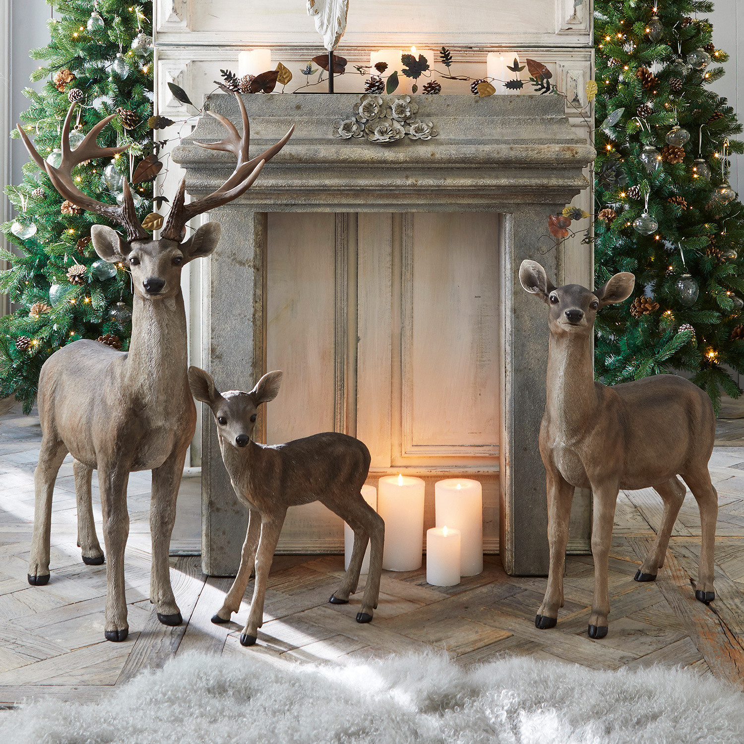 Cerf avec biche et faon Olsen Figurines décoratives de trois cerfs marron devant une cheminée avec bougies allumées et sapins décorés