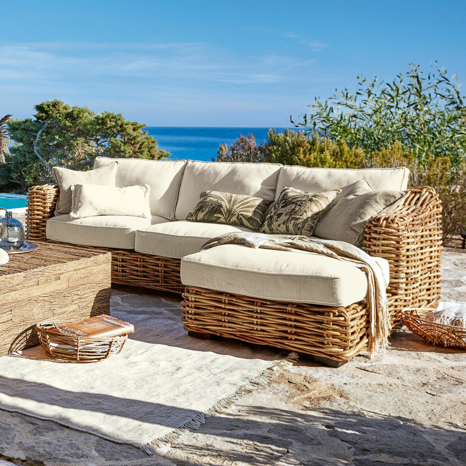 Canapé Villedieu Canapé d'angle en rotin avec coussins crème sur terrasse face à la mer, mobilier de jardin