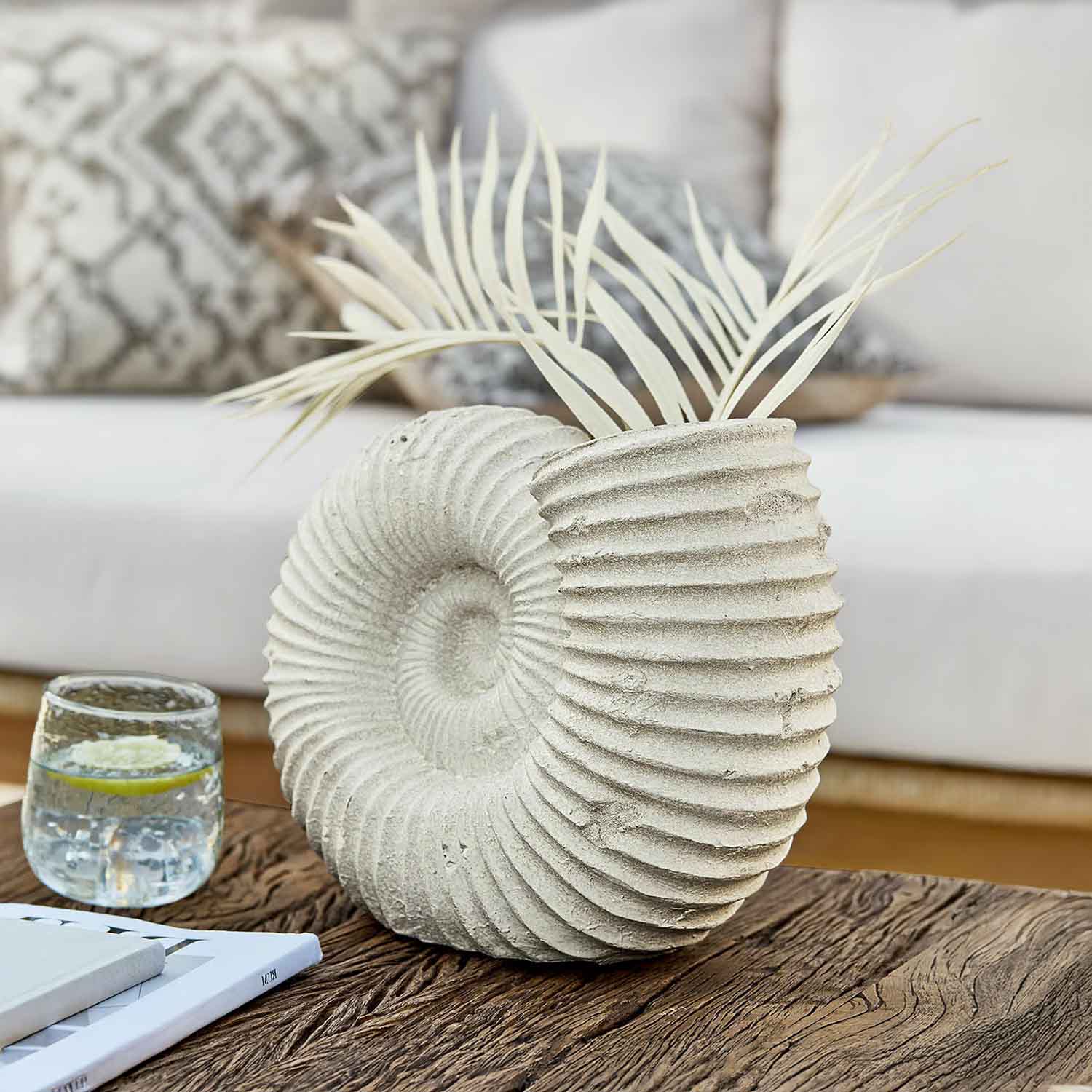 Vase décoratif en pierre claire en forme de coquillage avec feuilles séchées sur table en bois