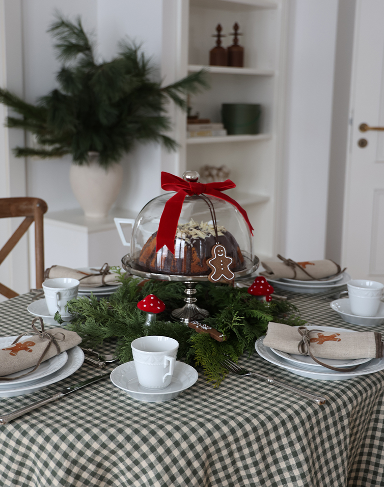 Table de fête avec gâteau sous cloche en verre, décorations de branches vertes et champignons rouges