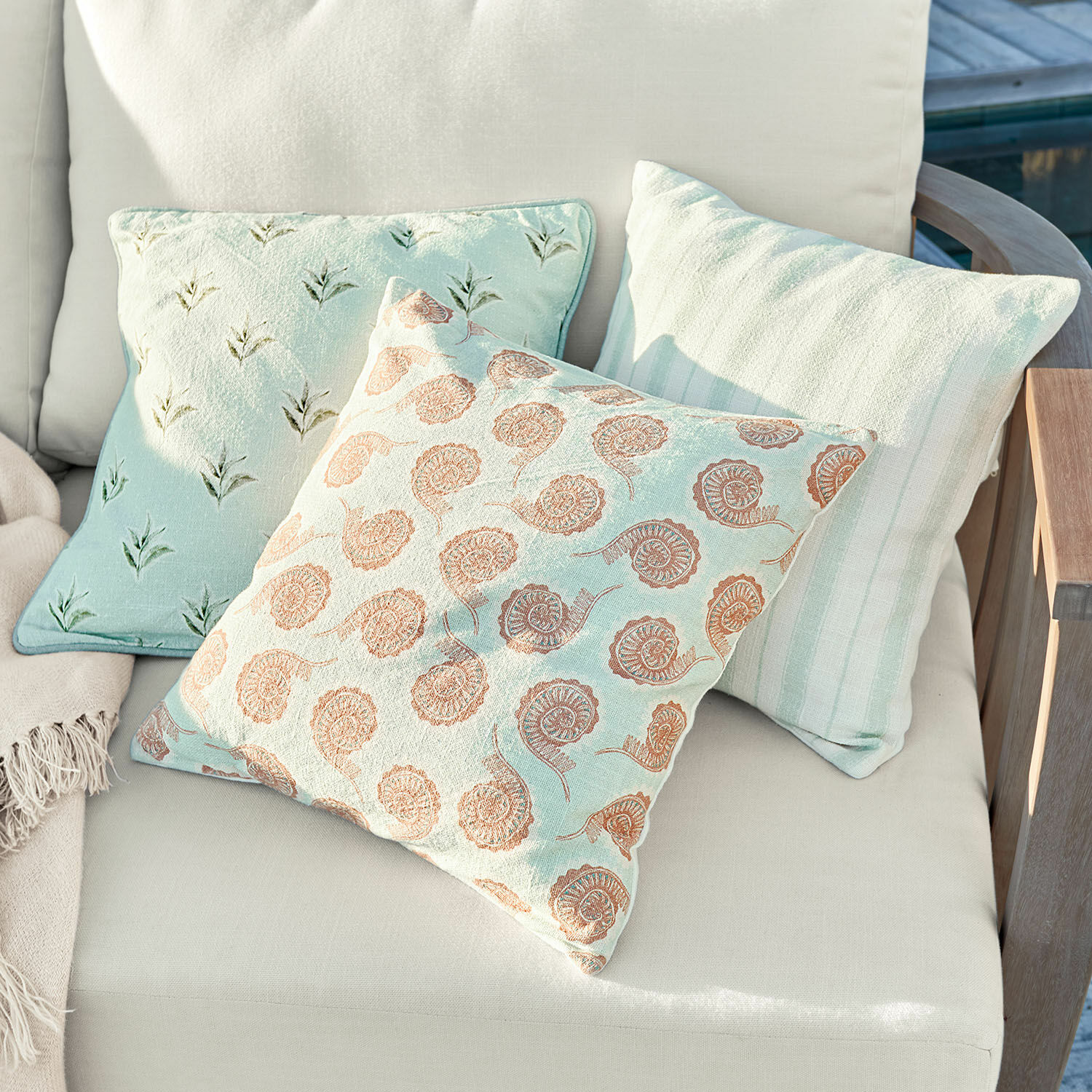Lot de 3 housses de coussin Père Trois coussins décoratifs pastel sur un canapé clair en tissu et bois pour salon extérieur