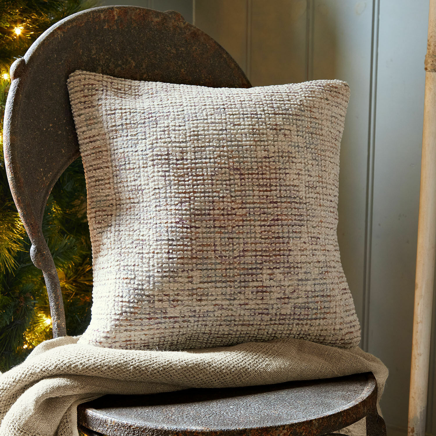 Housse de coussin Galavira Coussin décoratif beige en tissu texturé sur une chaise en métal rustique dans un intérieur chaleureux