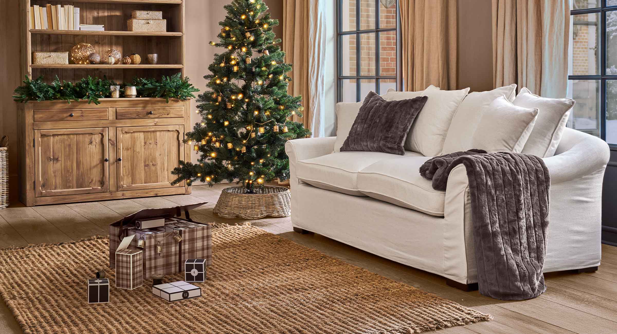 Salon chaleureux avec canapé blanc, coussins marron et sapin de Noël décoré de lumières