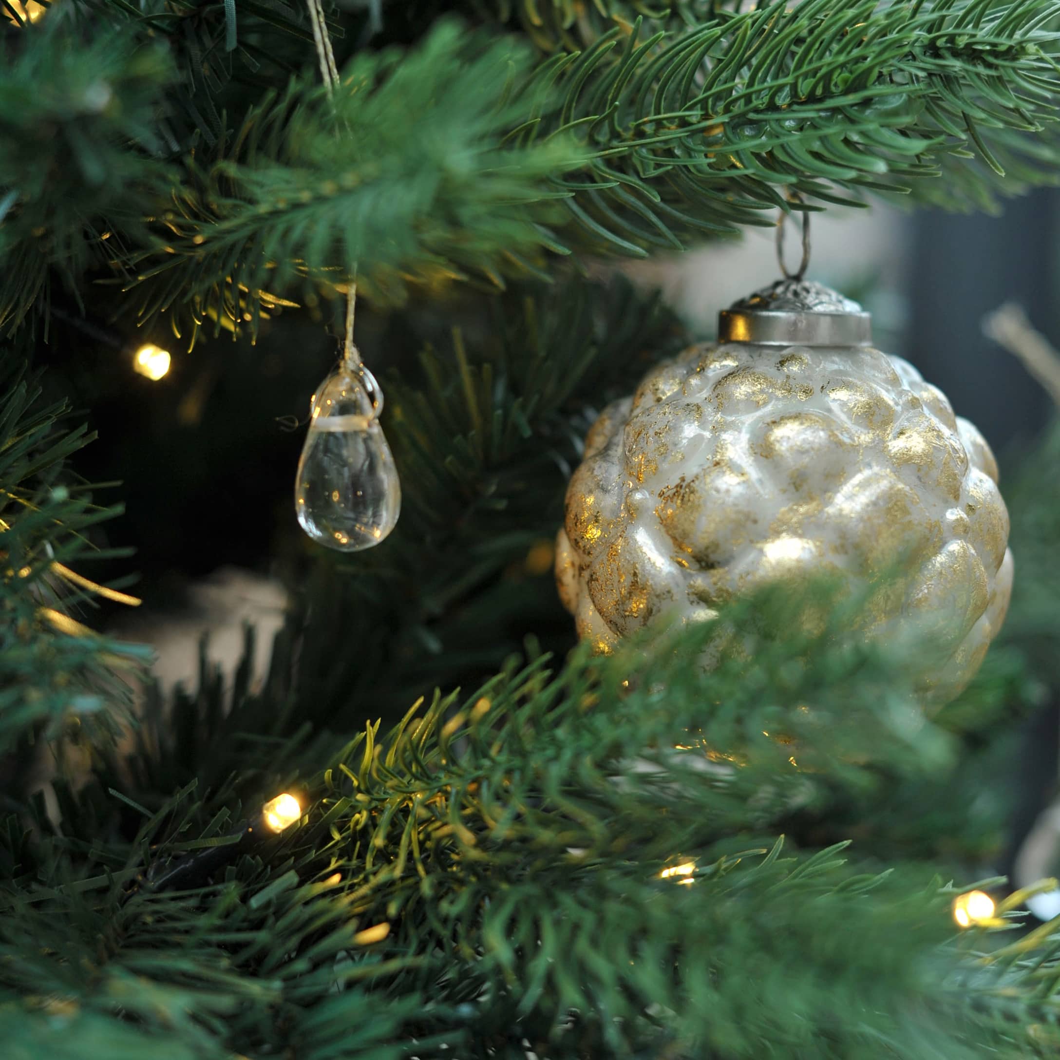 Gros plan sur une branche de sapin avec des décorations en verre transparent et doré pour Noël