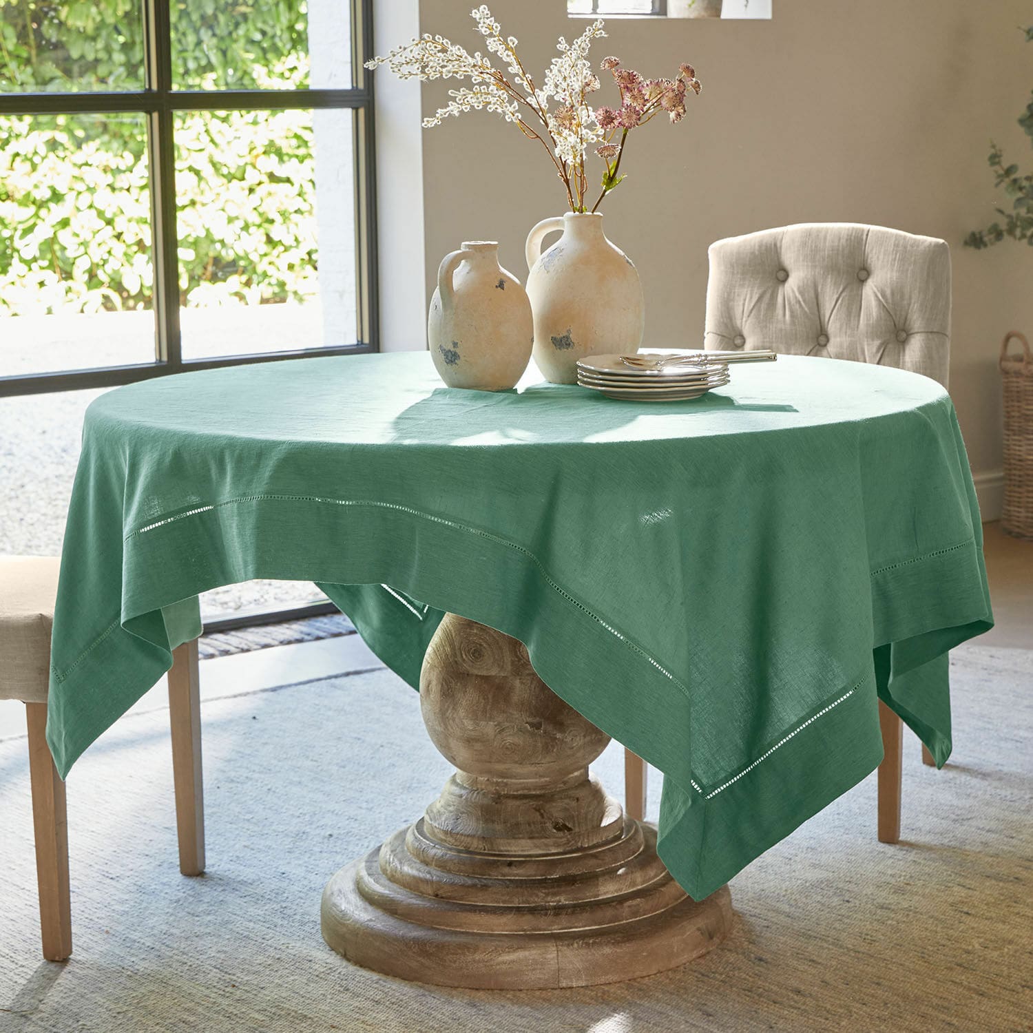 Nappe Covent Garden Table ronde avec pied en bois recouverte d'une nappe en lin vert avec détails ajourés décoratifs
