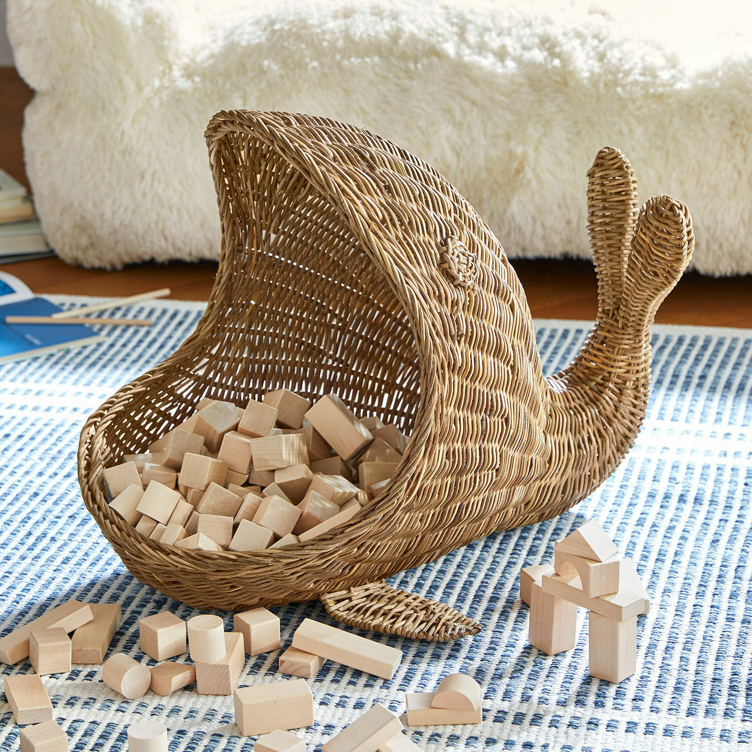 Corbeille Cheruboo Panier en forme de baleine en osier naturel avec blocs de bois sur un tapis à motifs bleus