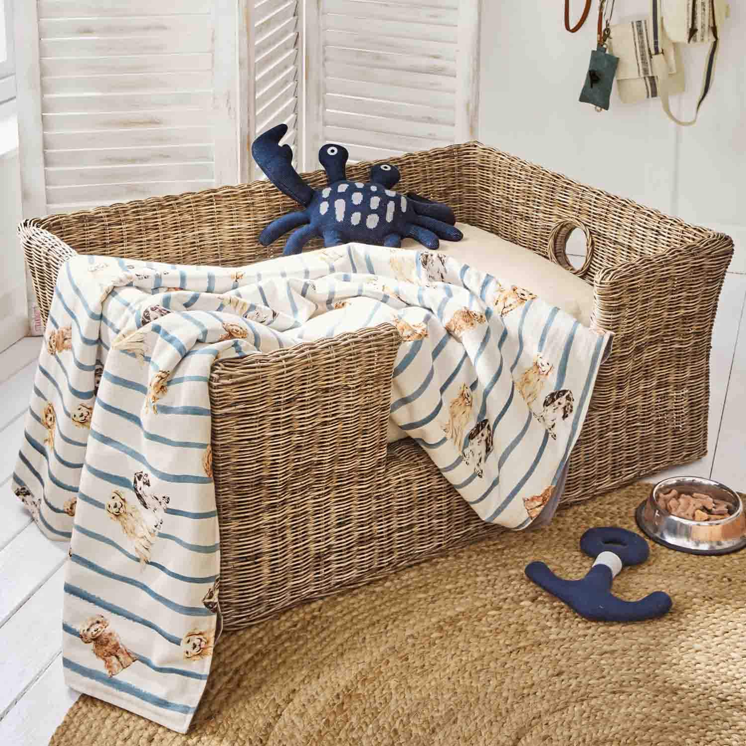 Panier en osier pour chien avec coussin crème, couverture rayée à motifs de chiens et jouet crabe bleu marine