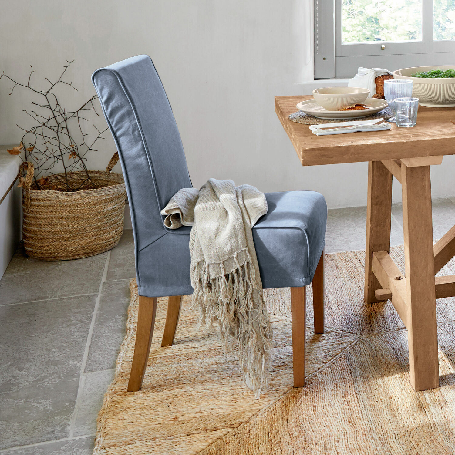 Chaise bleue rembourrée avec pieds en bois et plaid beige près d'une table en bois clair