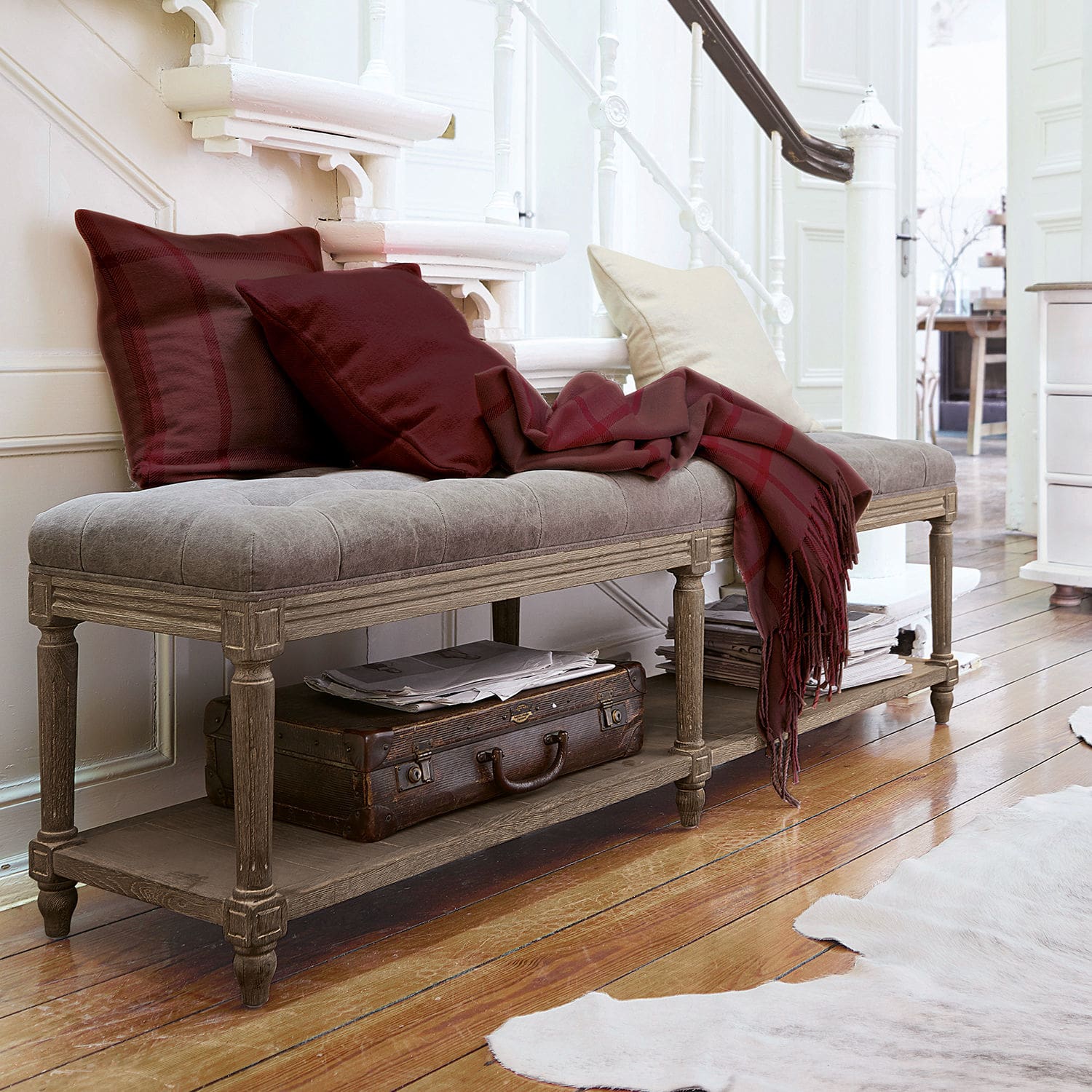 Banc Surcelles Banc rembourré gris avec cadre en bois, coussins bordeaux et plaid assorti dans un intérieur lumineux