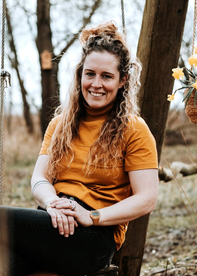 Femme en haut orange à manches courtes assise sur une balançoire dans un cadre naturel