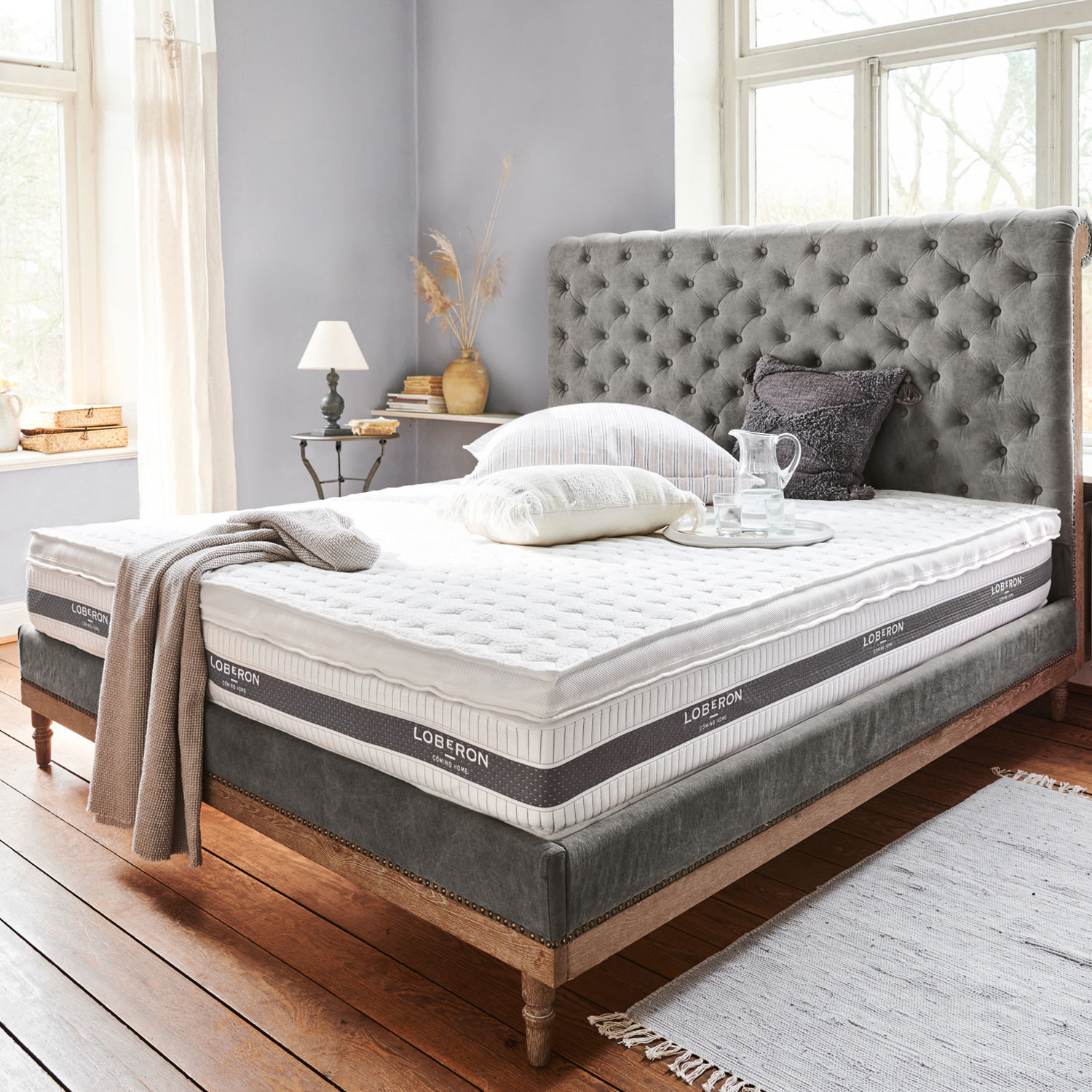 Surmatelas Danisar Lit avec tête de lit capitonnée grise et matelas blanc Loberon dans une chambre lumineuse et chaleureuse