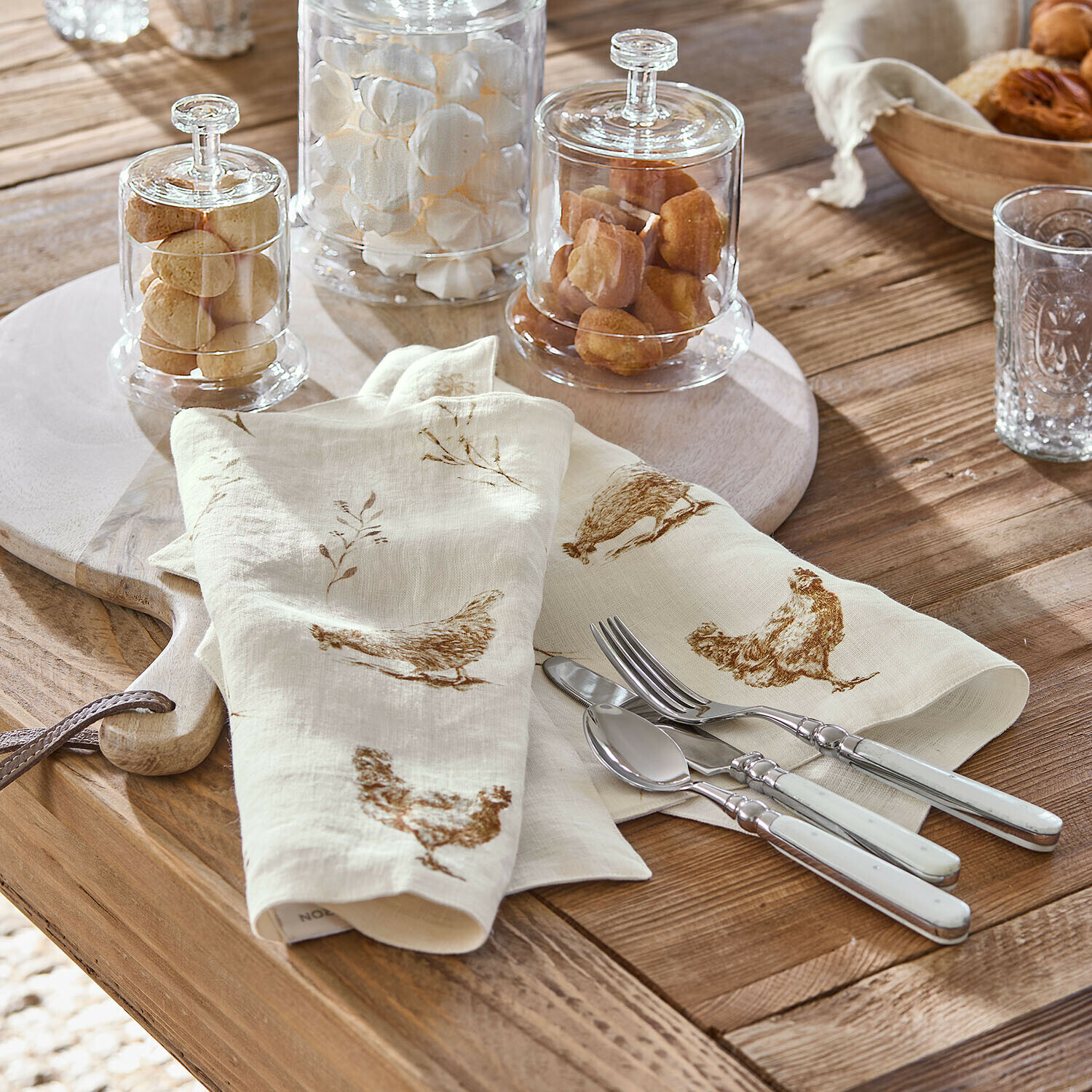 Lot de 2 sets de table Chavéreau Serviettes en lin crème avec imprimé poules marron sur table en bois avec couverts argentés