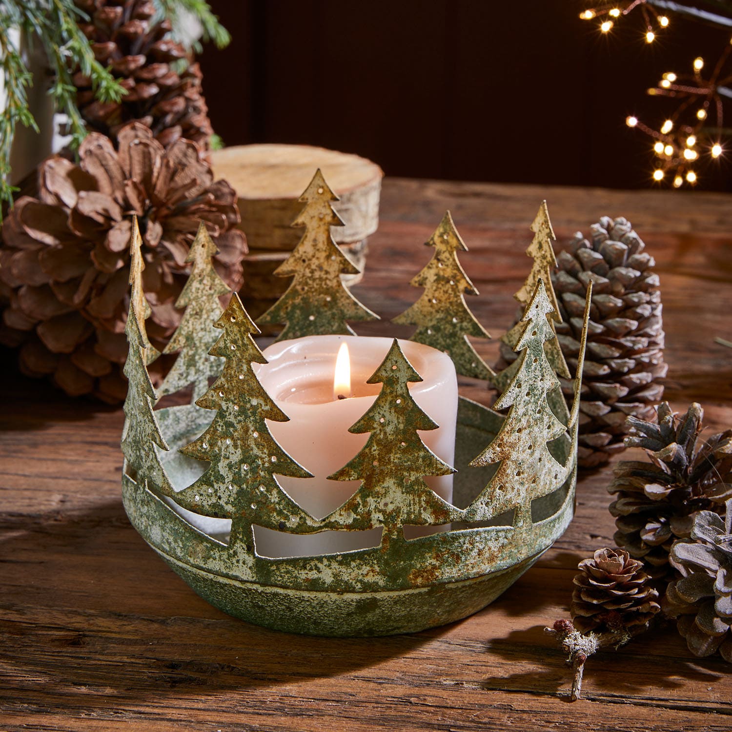 Bougeoir en métal vert patiné avec décor d'arbres de Noël et bougie blanche sur table en bois rustique