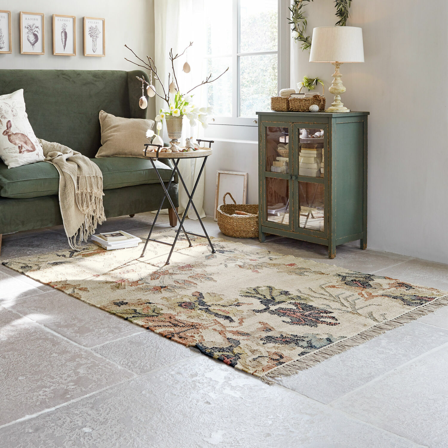 Tapis Osorno Salon chaleureux avec canapé vert, meuble en bois et tapis floral sur sol clair, décoration cosy