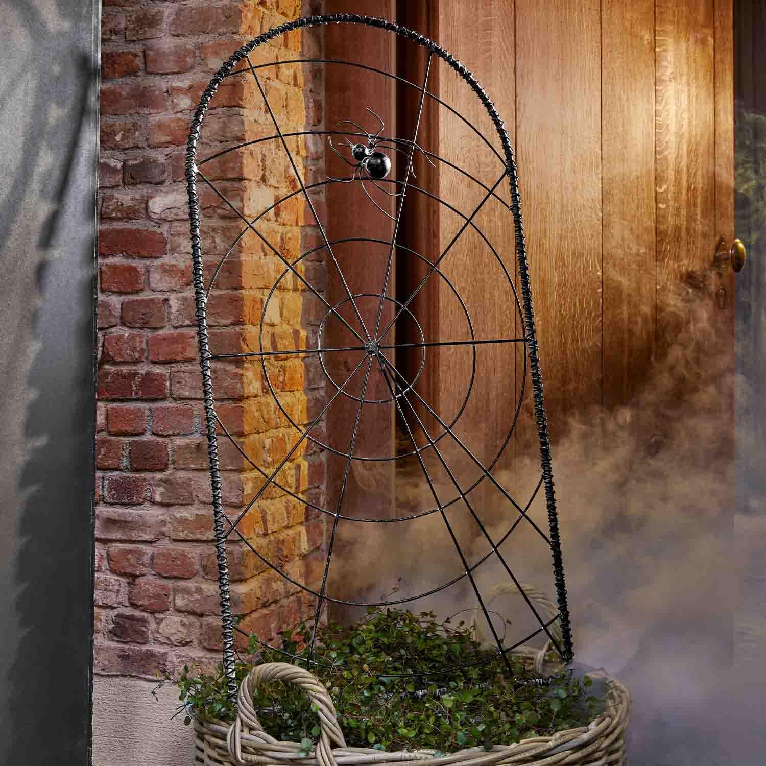 Décoration en métal noir en forme de toile d'araignée avec araignée devant un mur en briques et une porte en bois