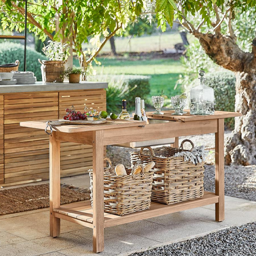 Table de jardin en bois naturel avec paniers en osier et accessoires de service sur terrasse ensoleillée
