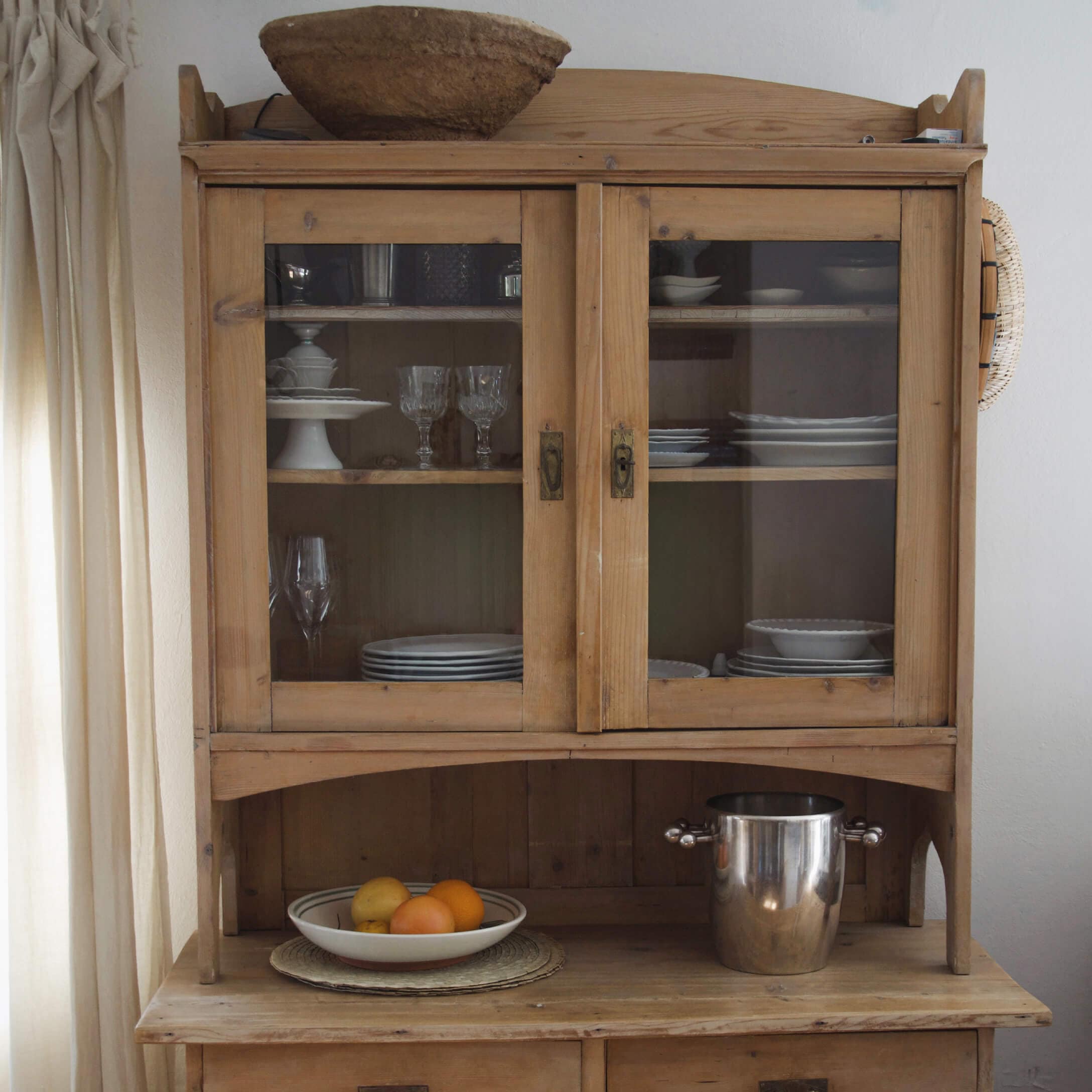 Buffet en bois avec portes vitrées, vaisselle blanche et seau en métal sur le dessus