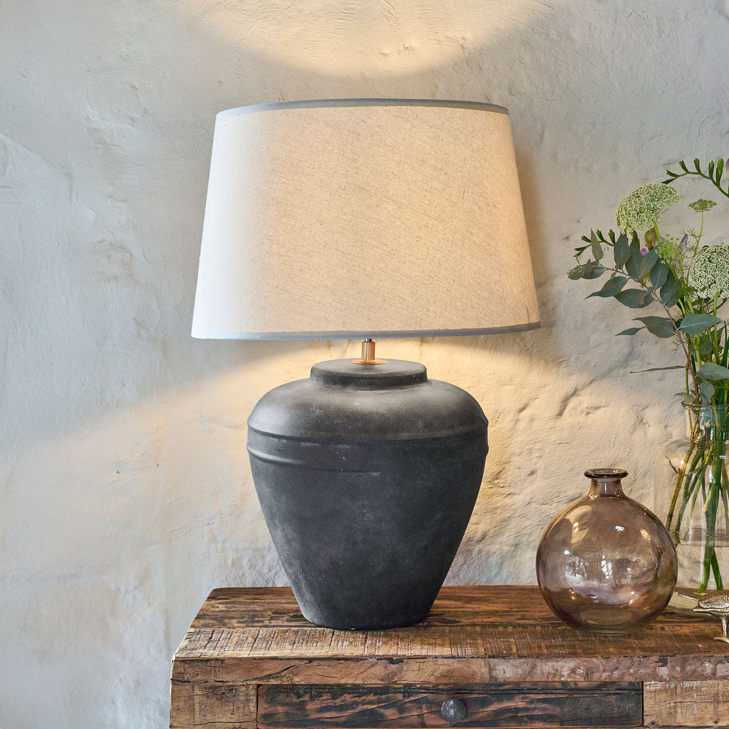 Lampe de table en céramique noire avec abat-jour beige posée sur une table en bois rustique