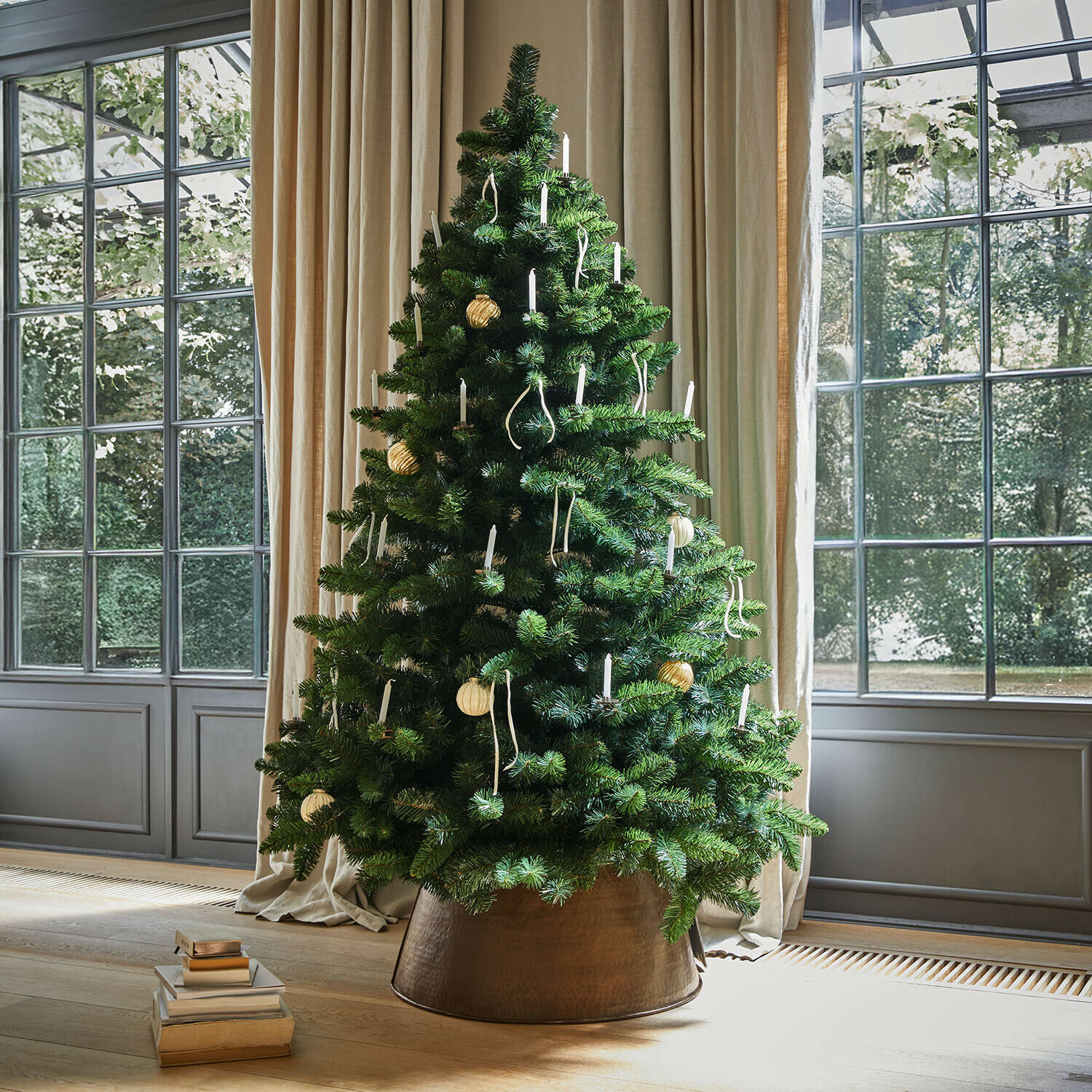 Arbre de Noël Bryndis Sapin artificiel vert décoré de bougies blanches dans un cache-pot en cuivre près d'une fenêtre lumineuse