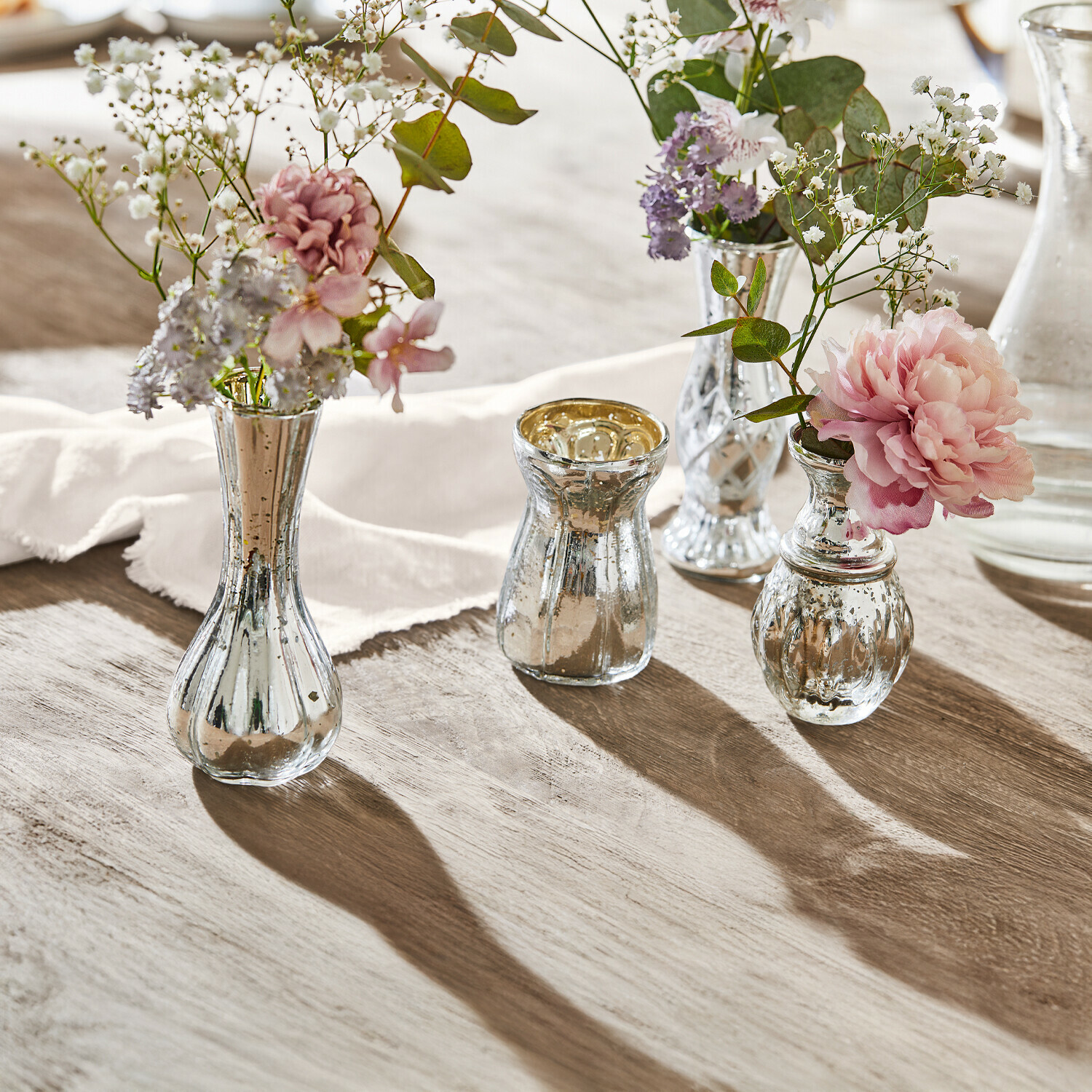 Lot de 4 vases décoratifs Maelie Ensemble de quatre vases en verre argenté avec fleurs sur table en bois, décoration élégante