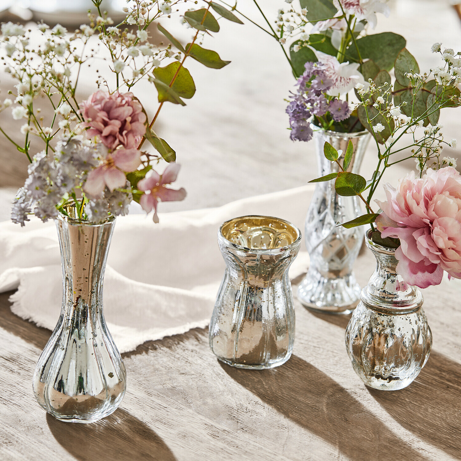 Lot de 4 vases décoratifs Maelie Ensemble de quatre vases en verre argenté avec fleurs sur table en bois, décoration élégante
