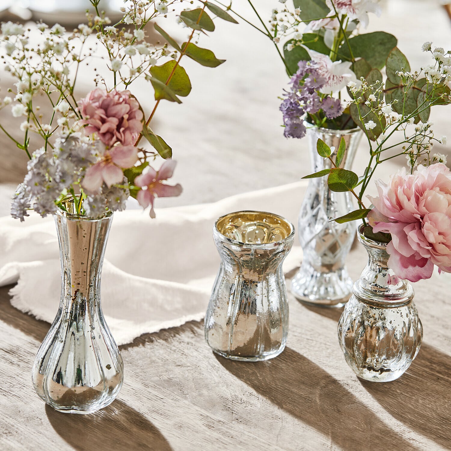 Lot de 4 vases décoratifs Maelie Ensemble de quatre vases en verre argenté avec fleurs sur table en bois, décoration élégante