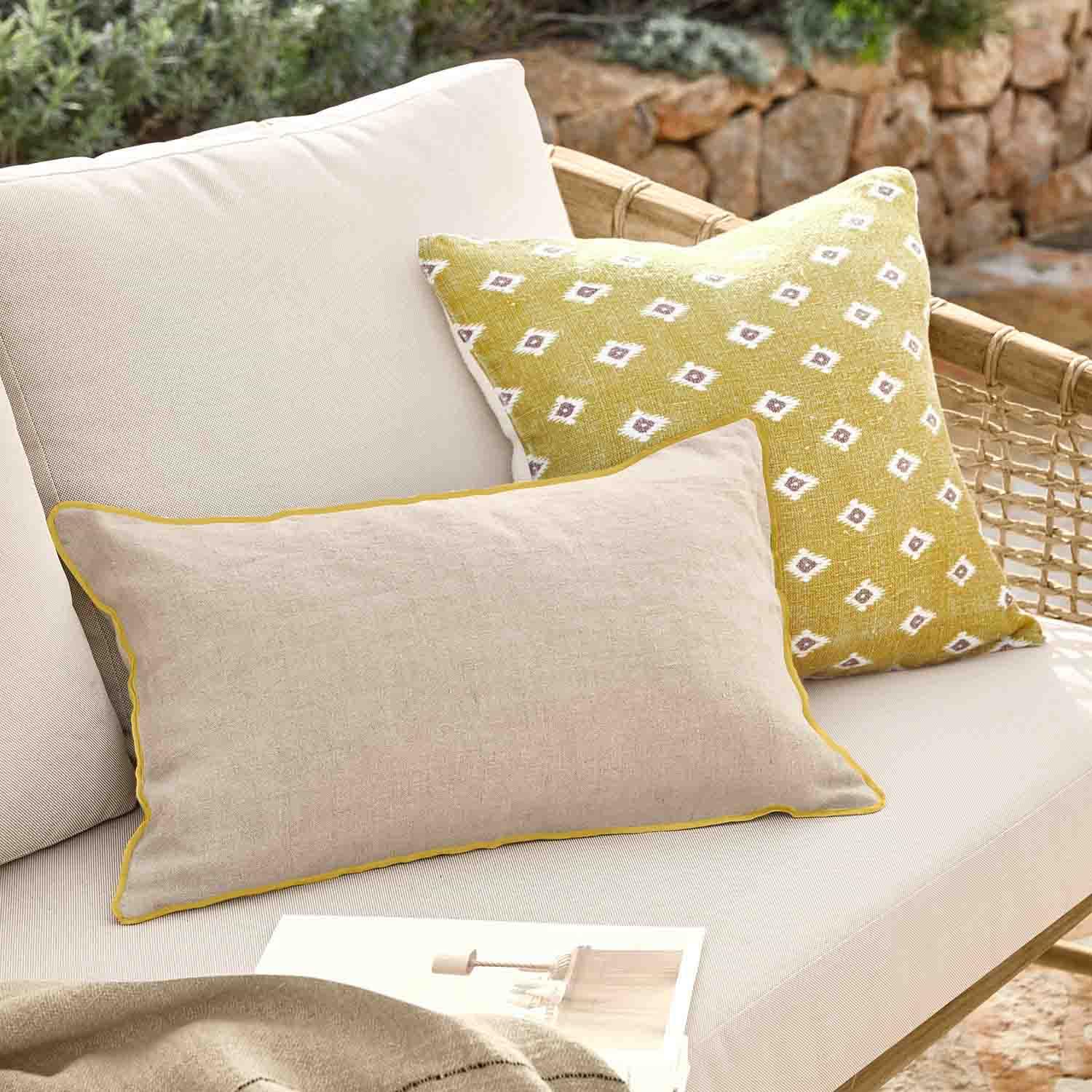 Coussin beige avec bordure jaune et coussin jaune à motifs blancs sur canapé en rotin extérieur