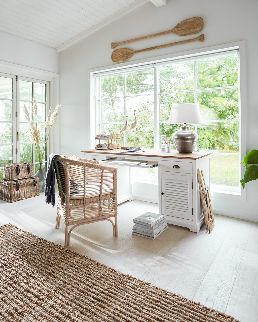 Bureau en bois blanc avec plateau naturel et chaise en osier dans une pièce lumineuse avec grande fenêtre