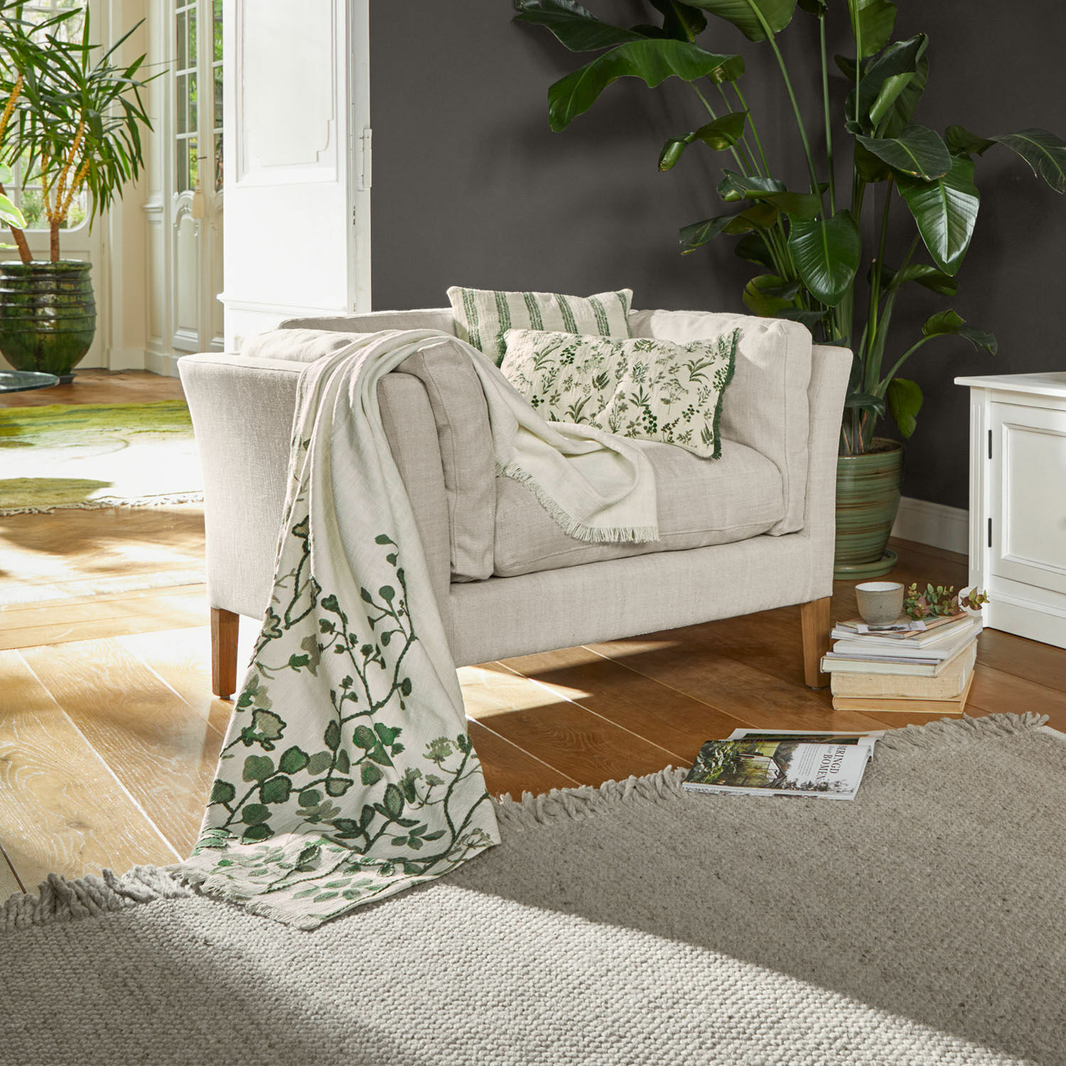 Fauteuil Lourvière Canapé beige en tissu avec coussins verts et plaid à motif végétal dans un salon lumineux