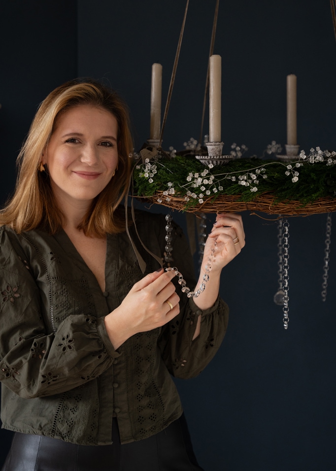 Femme décorant une couronne de l'Avent verte avec des bougies blanches et des décorations en cristal