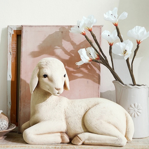 Figurine décorative d'agneau clair posée près d'un vase avec des fleurs blanches, décoration intérieure