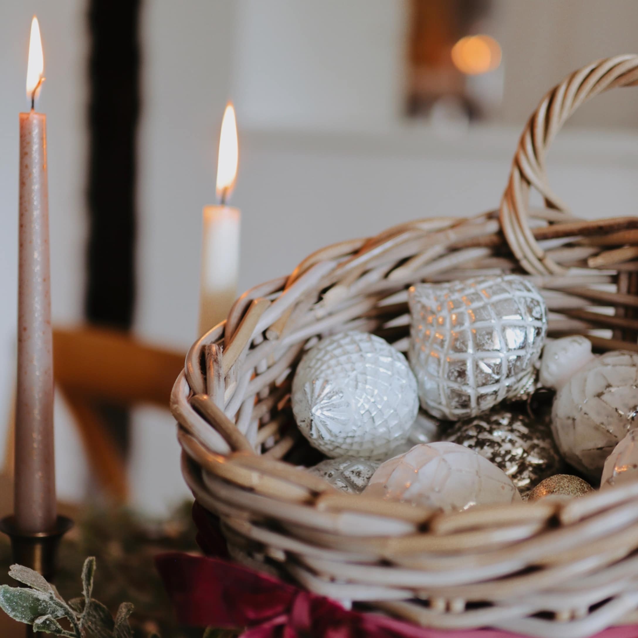 Panier en osier avec décorations de Noël argentées et blanches, bougies allumées en arrière-plan
