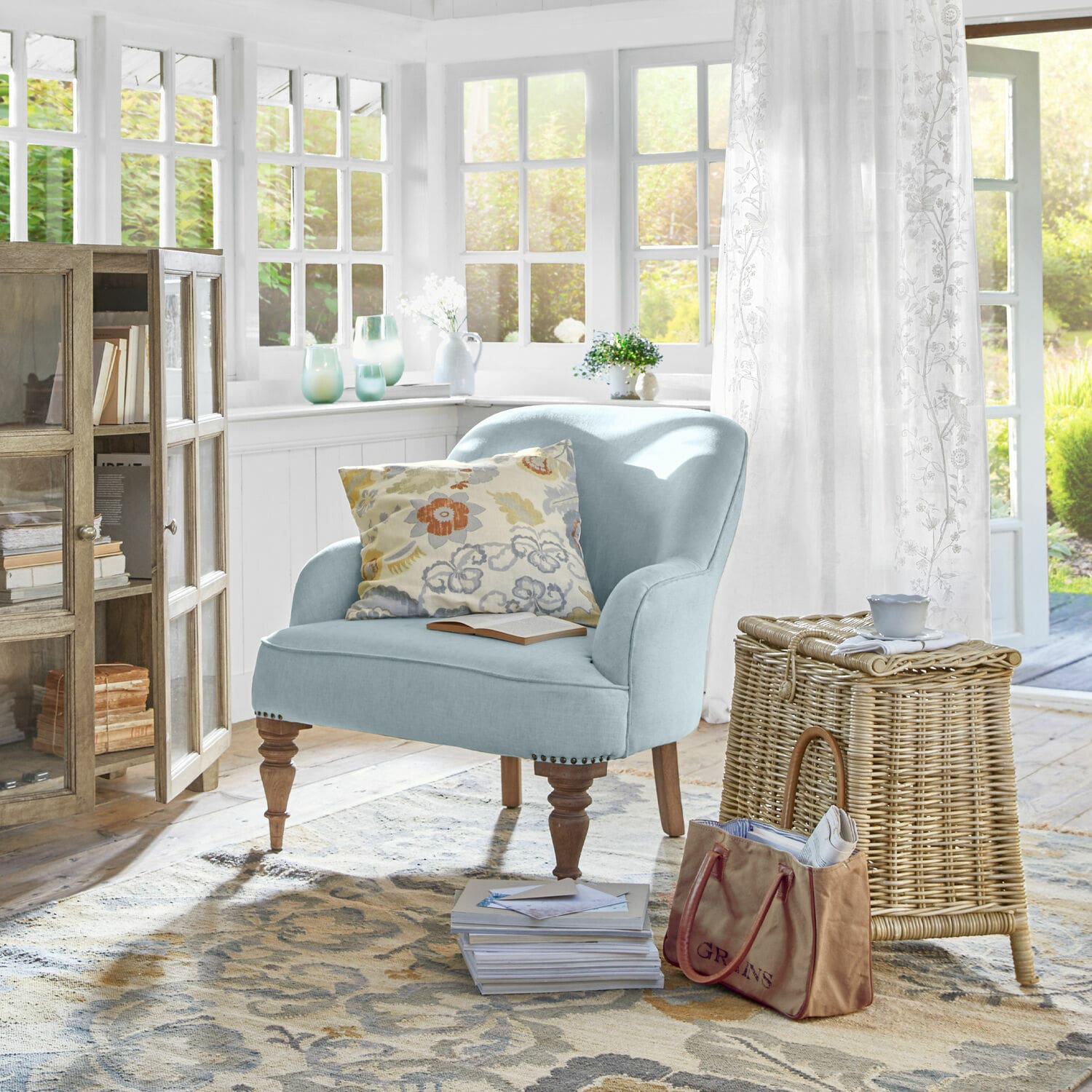Fauteuil Ainsley Fauteuil tapissé bleu clair avec pieds en bois dans un salon lumineux avec panier en osier et coussin floral